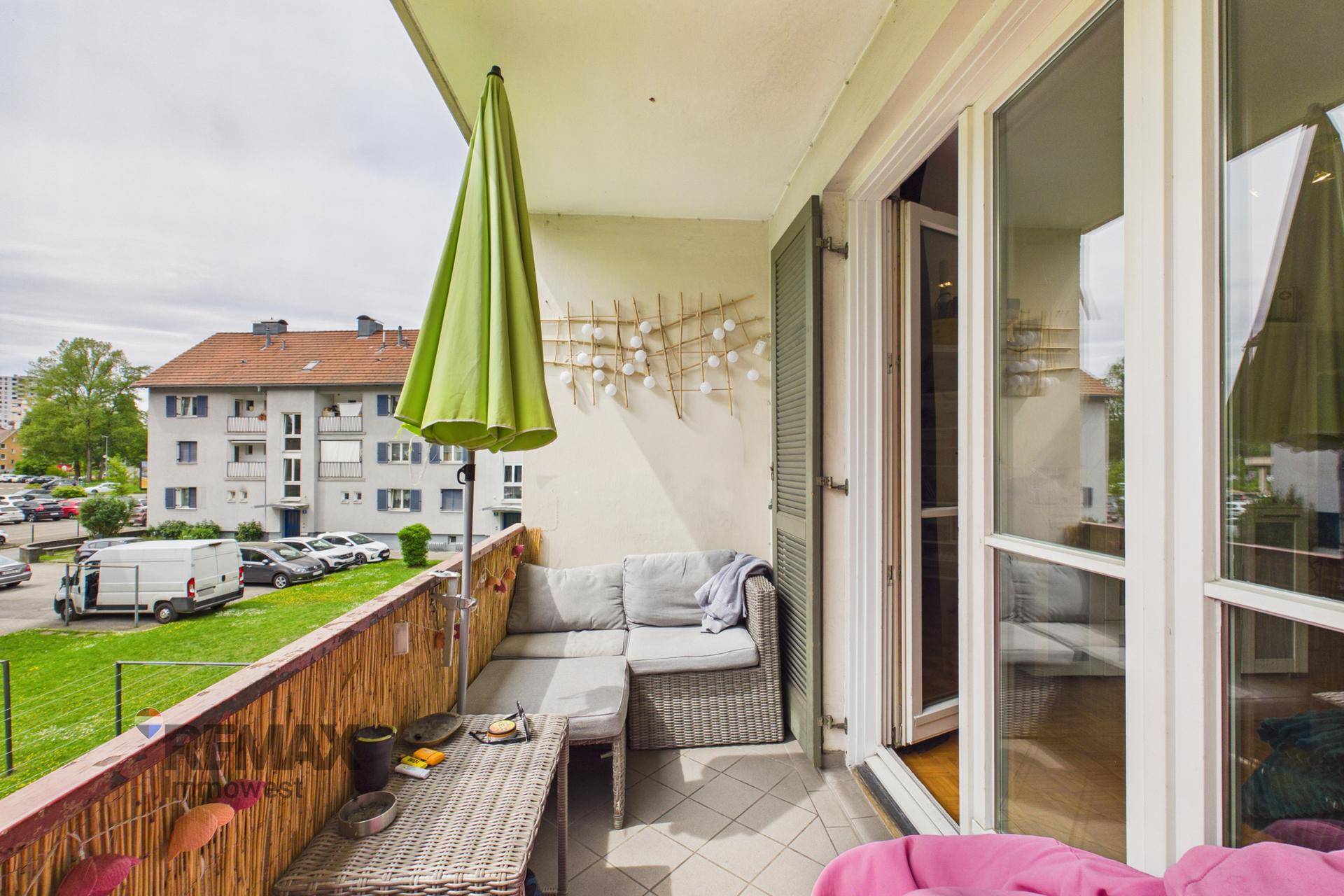 Möblierter Balkon mit Sonnenschirm und Blick auf die Grünfläche und Umgebung.