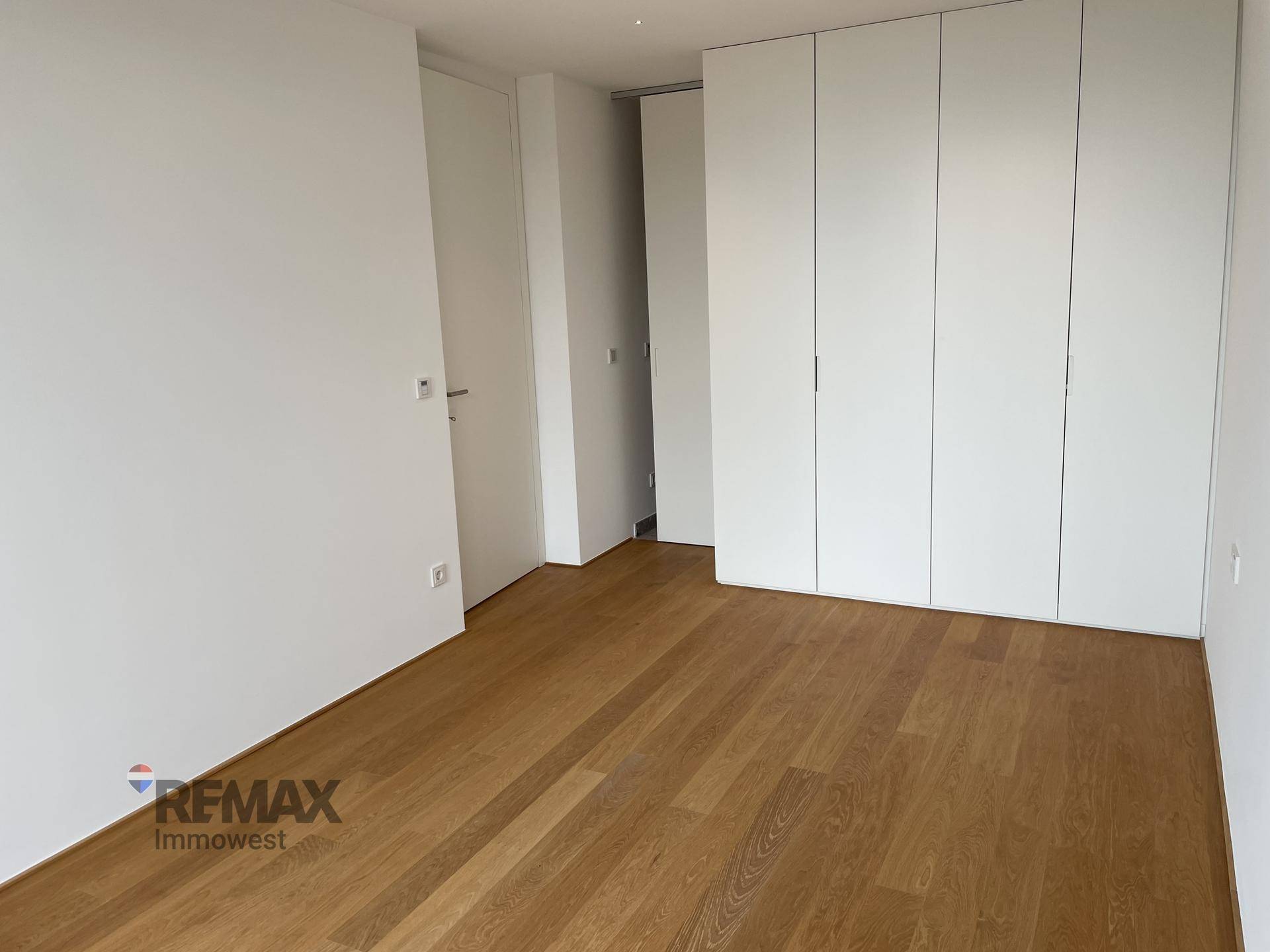 Helles Schlafzimmer mit Eichenparkettboden und praktischen Einbauschränken in Weiß.