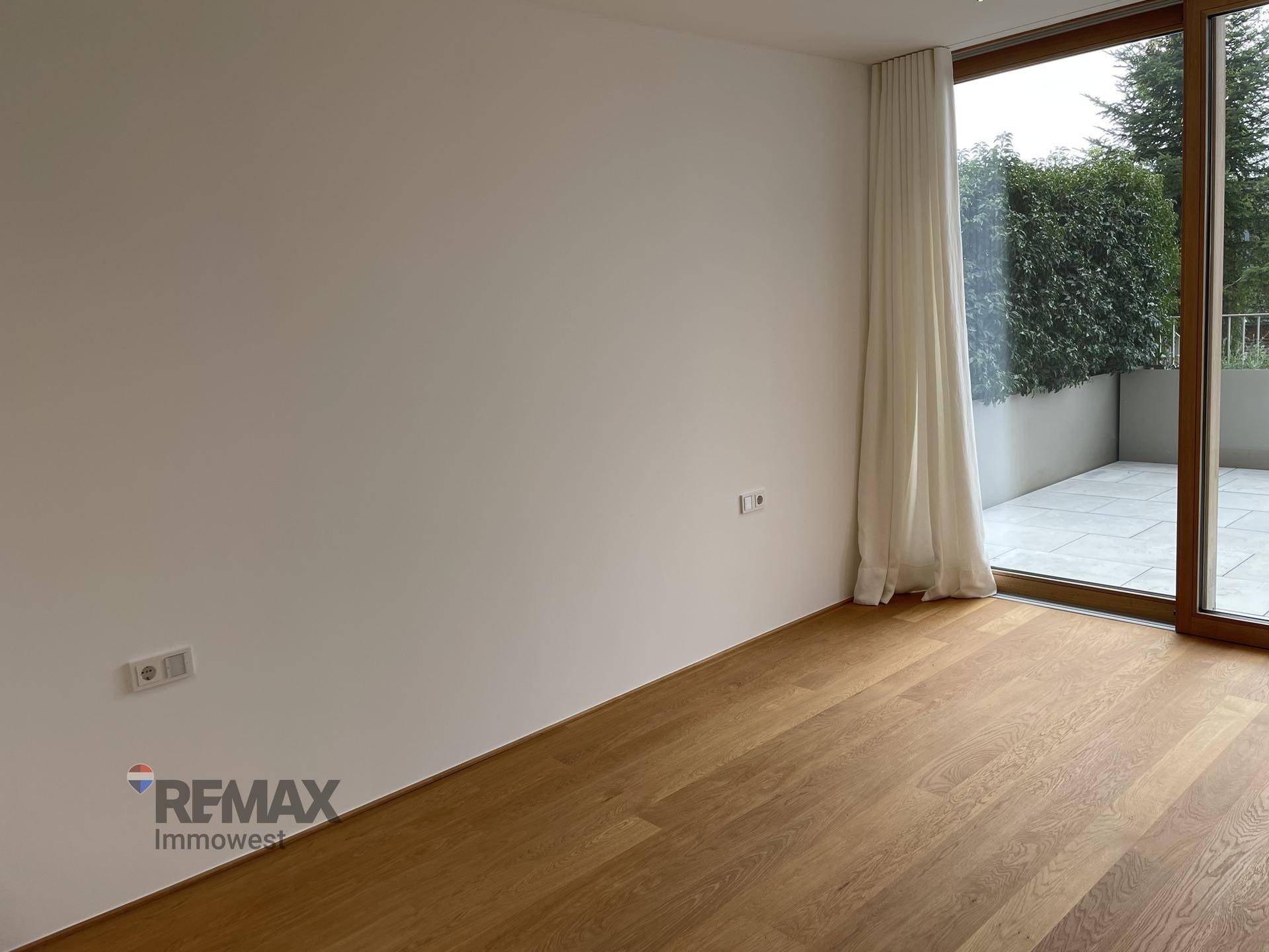Geräumiges Wohnzimmer mit Holzboden und großer Schiebetür, die auf eine Terrasse führt.