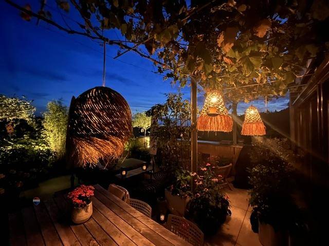 Stimmungsvoll beleuchtete Terrasse am Abend mit Esstisch, Pflanzen und gemütlicher Atmosphäre.