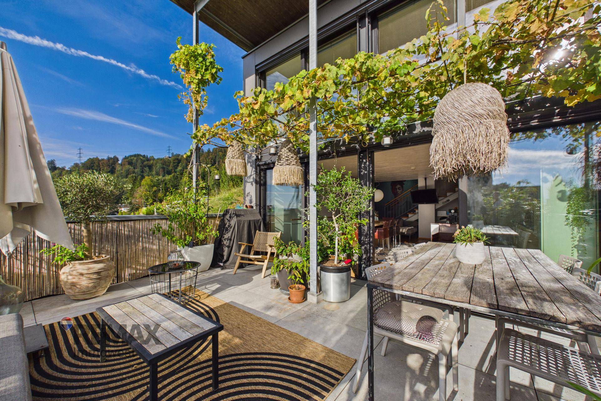 Weitläufige Terrasse mit verschiedenen Sitzbereichen, üppiger Bepflanzung und Fernblick.