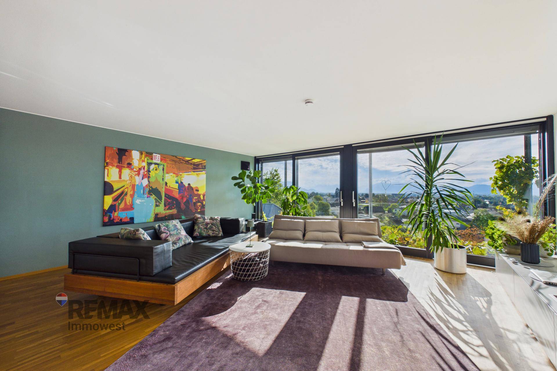 Helles Wohnzimmer mit bequemen Sofas, Holzboden und großen Fenstern mit Panoramablick.