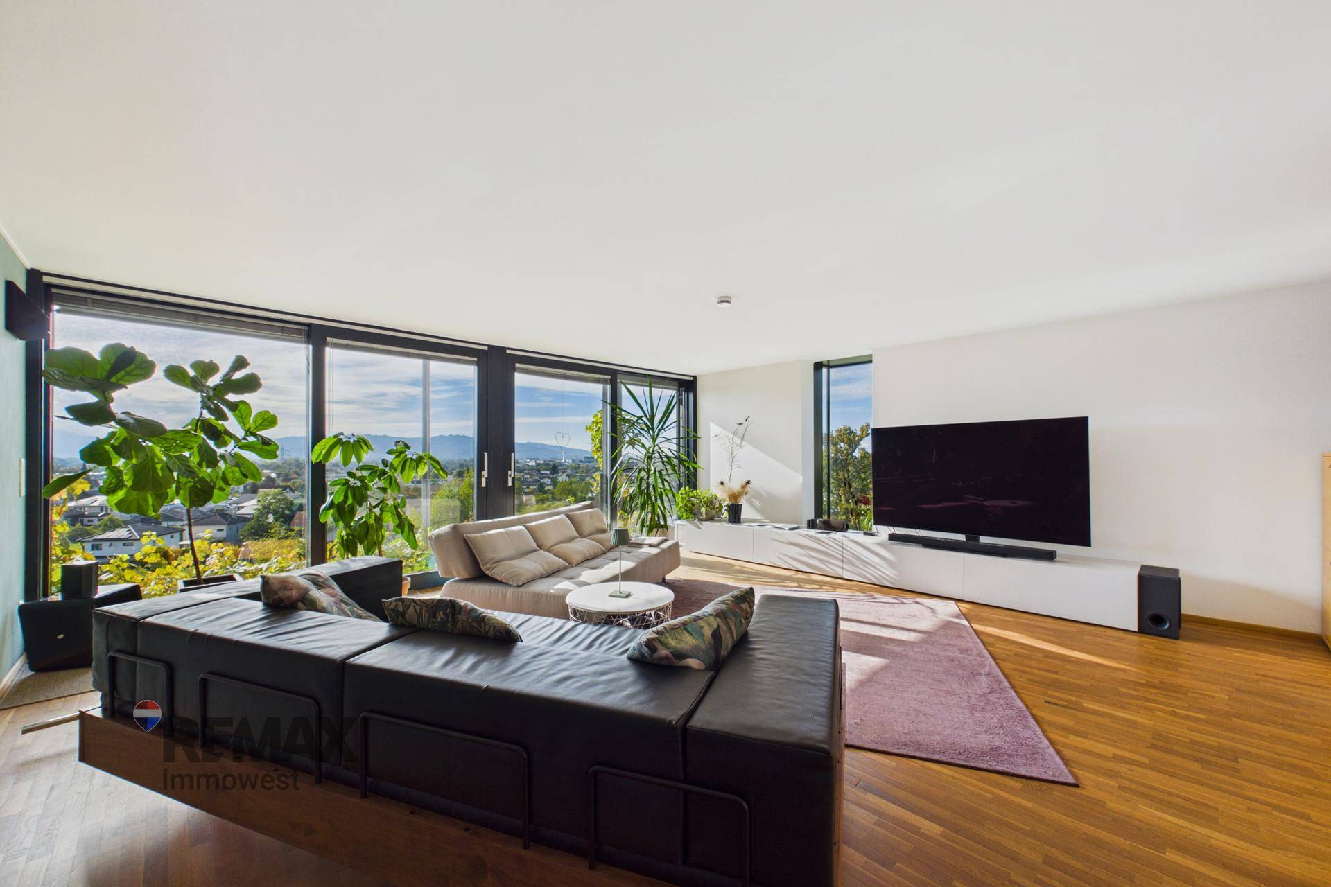 Großzügiges Wohnzimmer mit bodentiefen Fenstern, Holzboden und weitem Blick in die Landschaft.