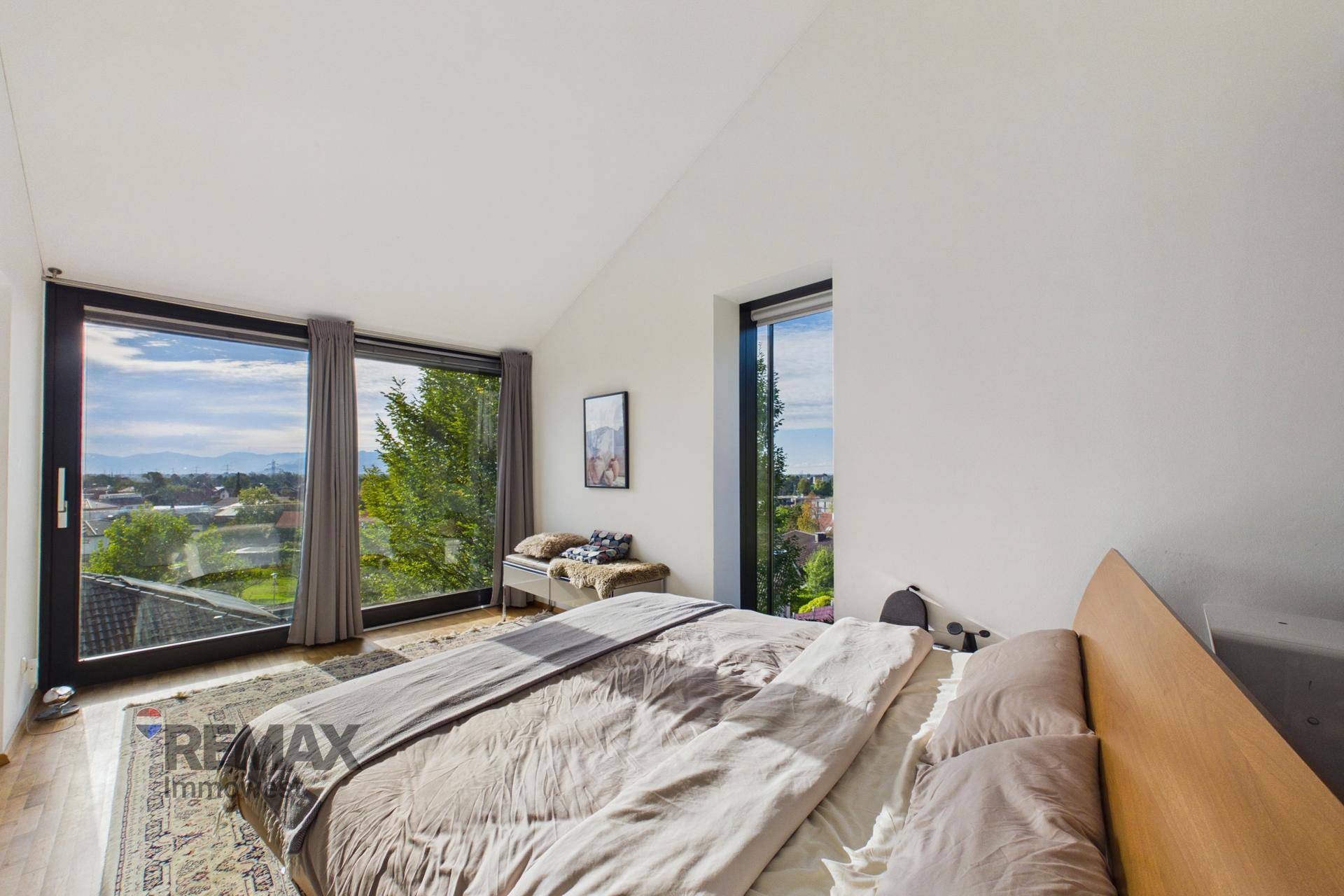 Helles Schlafzimmer mit großen Fenstern, Holzboden und weitem Blick auf die Umgebung.