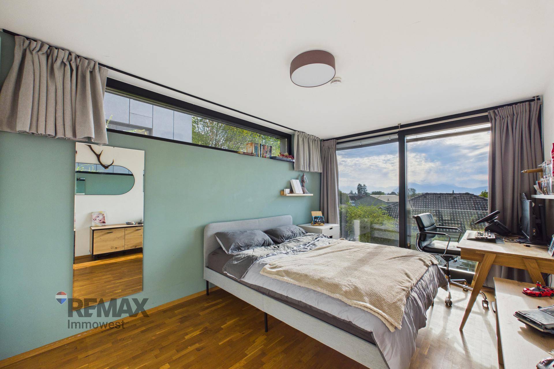 Schlafzimmer mit Holzboden, Schreibtisch und großen Fenstern mit Blick auf die Landschaft.