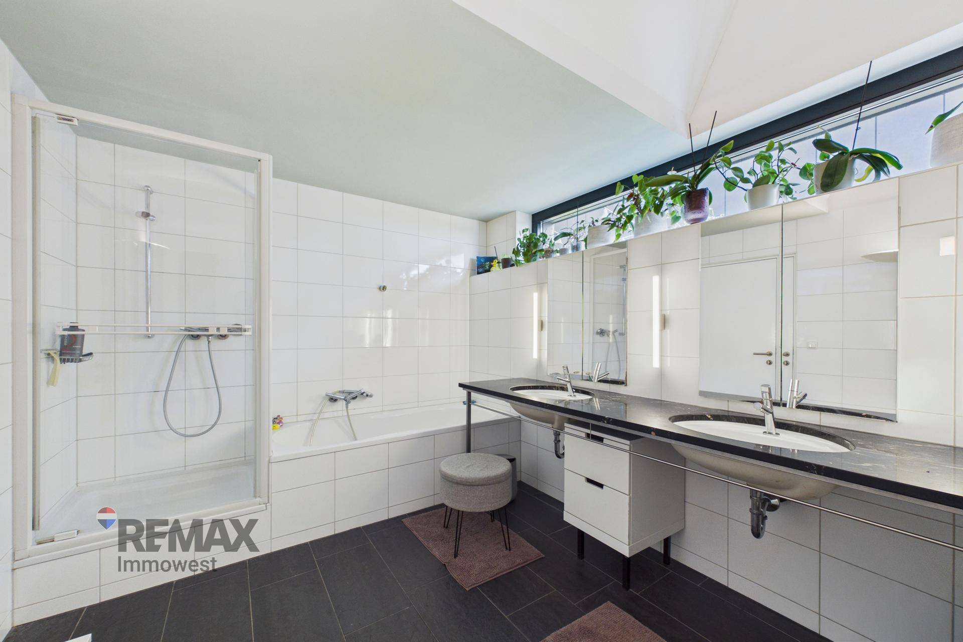 Helles Badezimmer mit Badewanne, Duschkabine, Doppelwaschbecken und großem Fenster.