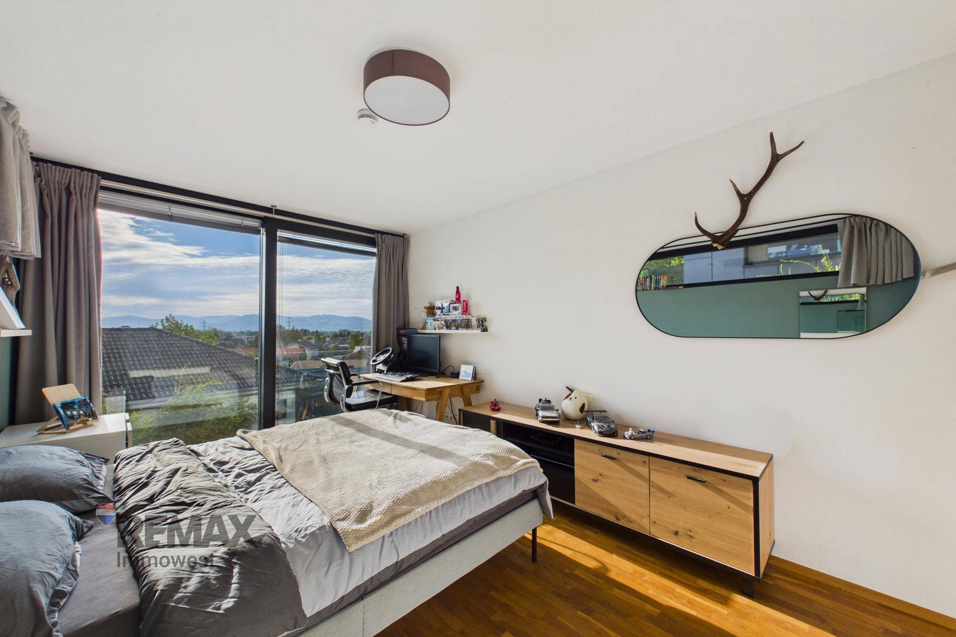 Helles Schlafzimmer mit Holzboden, Kommode und großen Fenstern mit Panoramablick.