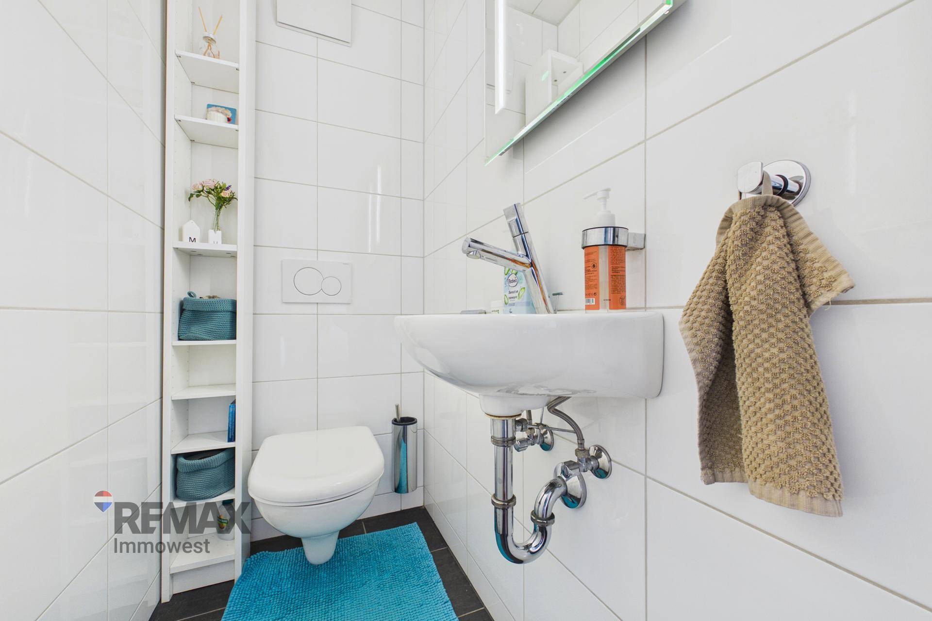 Modernes Gäste-WC mit wandhängender Toilette, kleinem Waschbecken und weißen Fliesen.