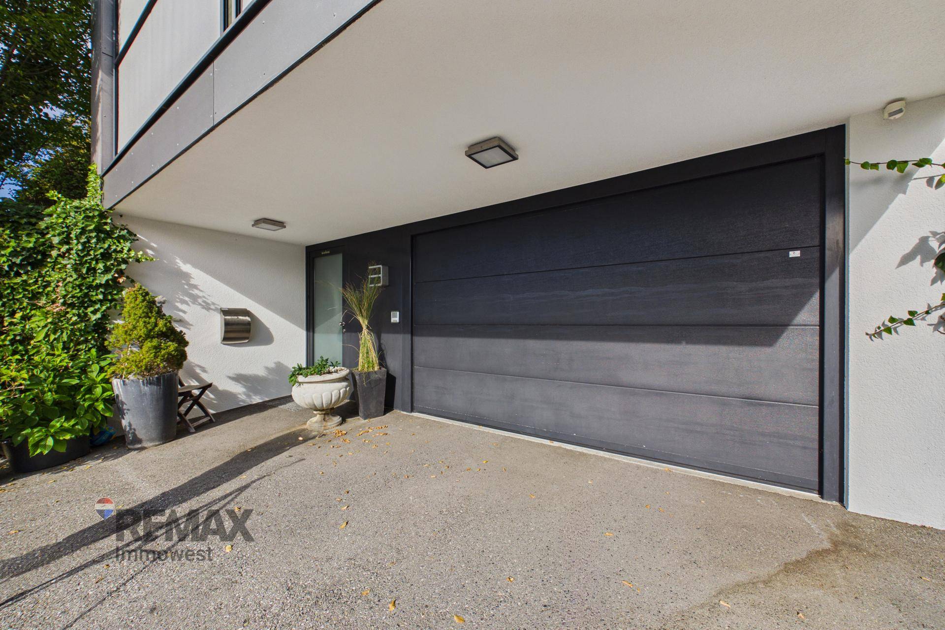 Moderner Garagenzugang mit dunklem Tor und gepflegter Bepflanzung am Eingangsbereich.