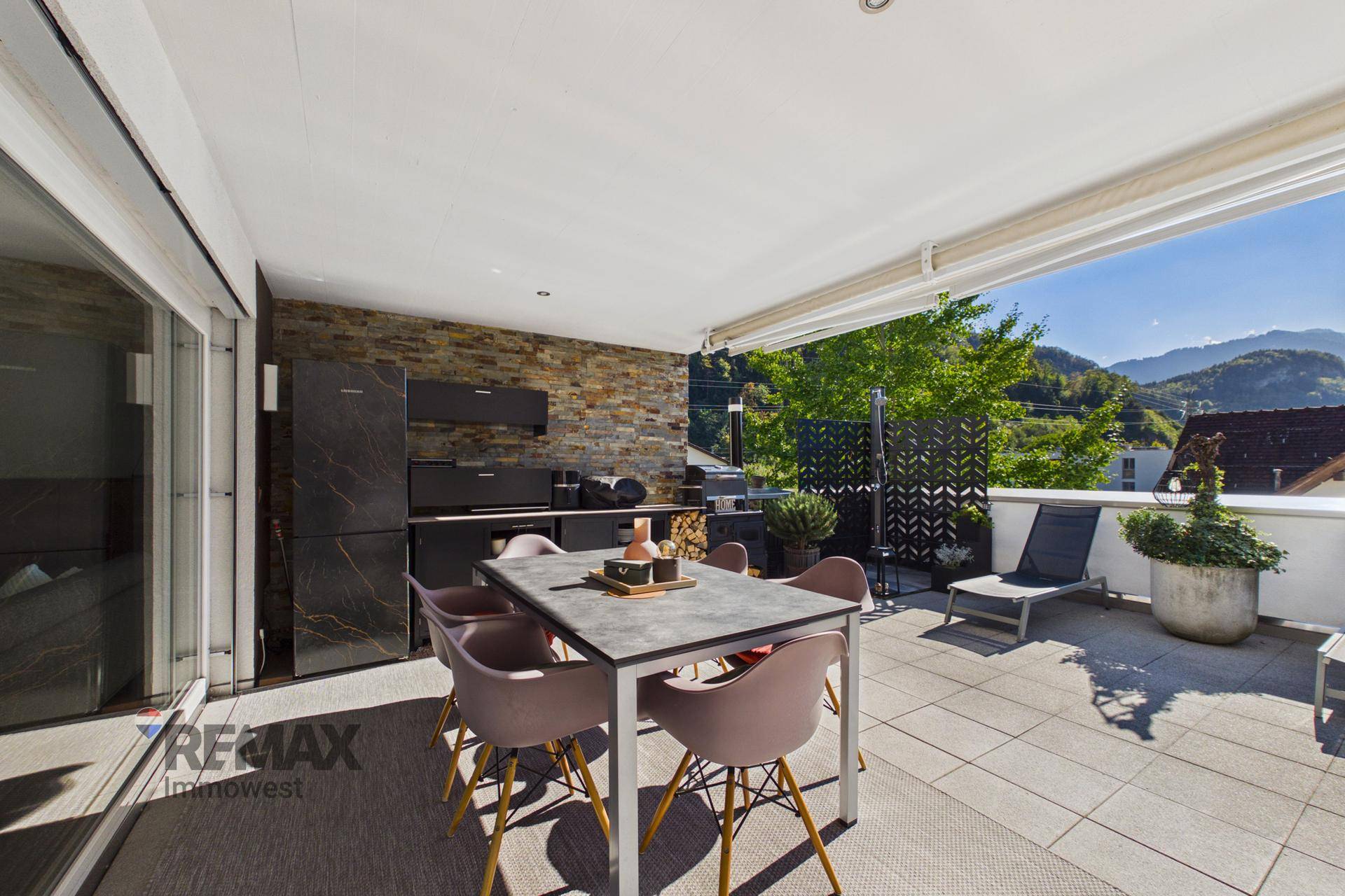 Sonnige Terrasse mit Außenküche, Essbereich und Steinwand, ideal für gesellige Abende.