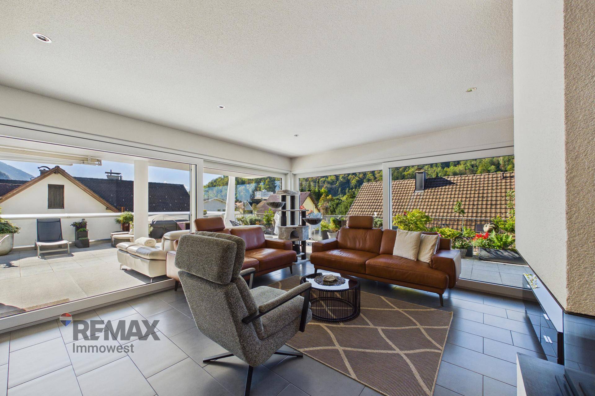 Geräumiges Wohnzimmer mit bequemen Ledersofas, großzügigen Fenstern und Blick auf die Terrasse.