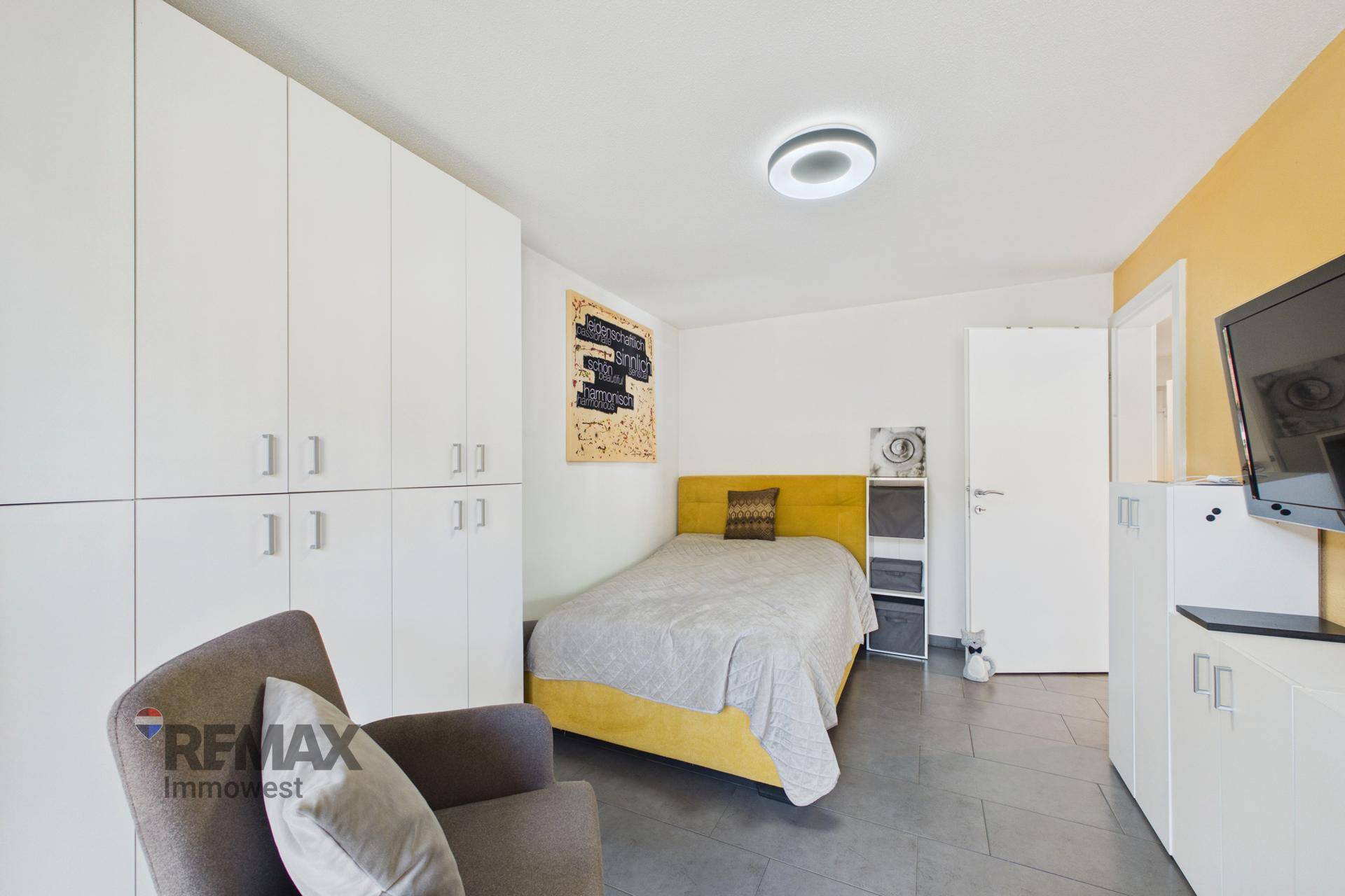 Gemütliches Schlafzimmer mit Einzelbett, Einbauschränken und einem Sessel, in hellen Farben gehalten.