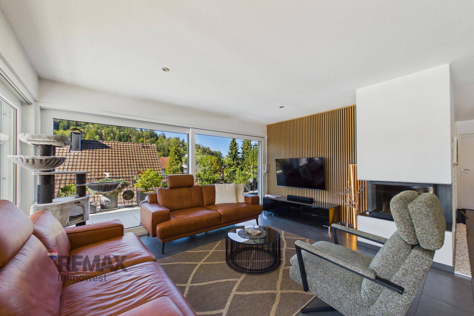 Gemütliches Wohnzimmer mit Kamin, Ledersofas und großen Fenstern mit Blick ins Grüne.