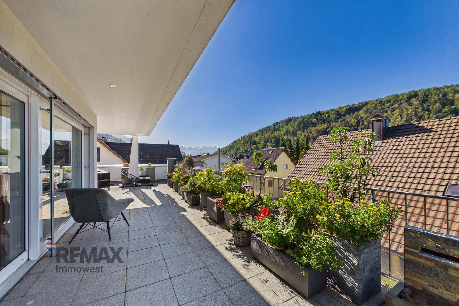 Langer Balkon mit Pflanzenkübeln und einem Stuhl, bietet einen schönen Blick auf die Berge.