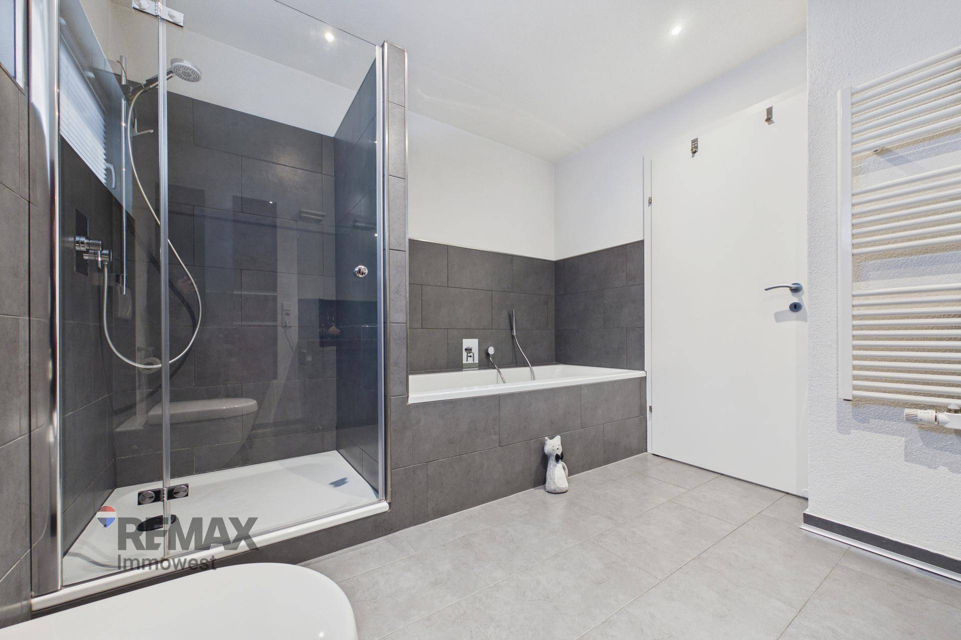 Geräumiges Badezimmer mit Badewanne, separater Dusche und beheiztem Handtuchhalter, in modernen Grautönen.