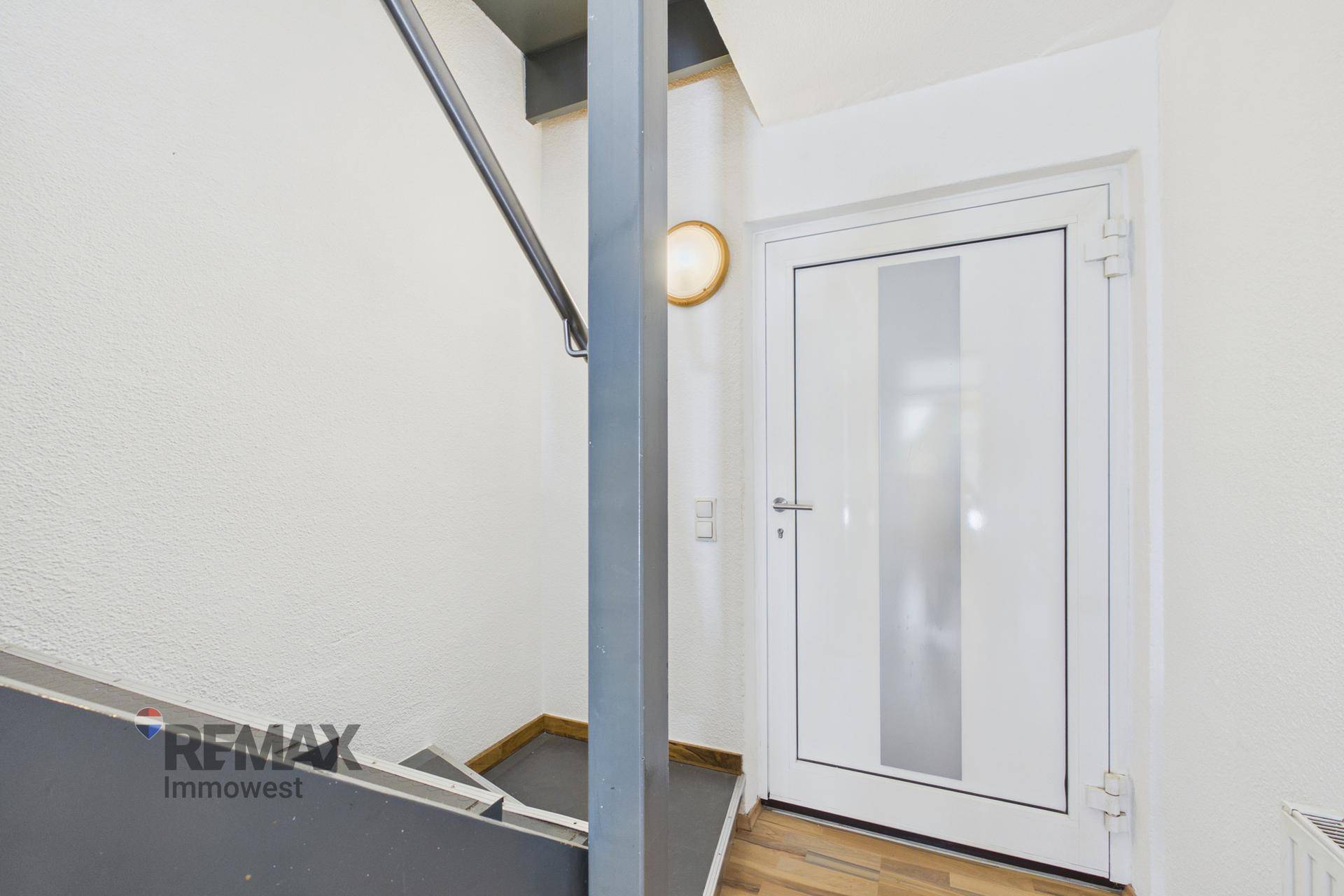 Heller Eingangsbereich mit Treppe und moderner Tür, die zu den oberen Etagen führt.