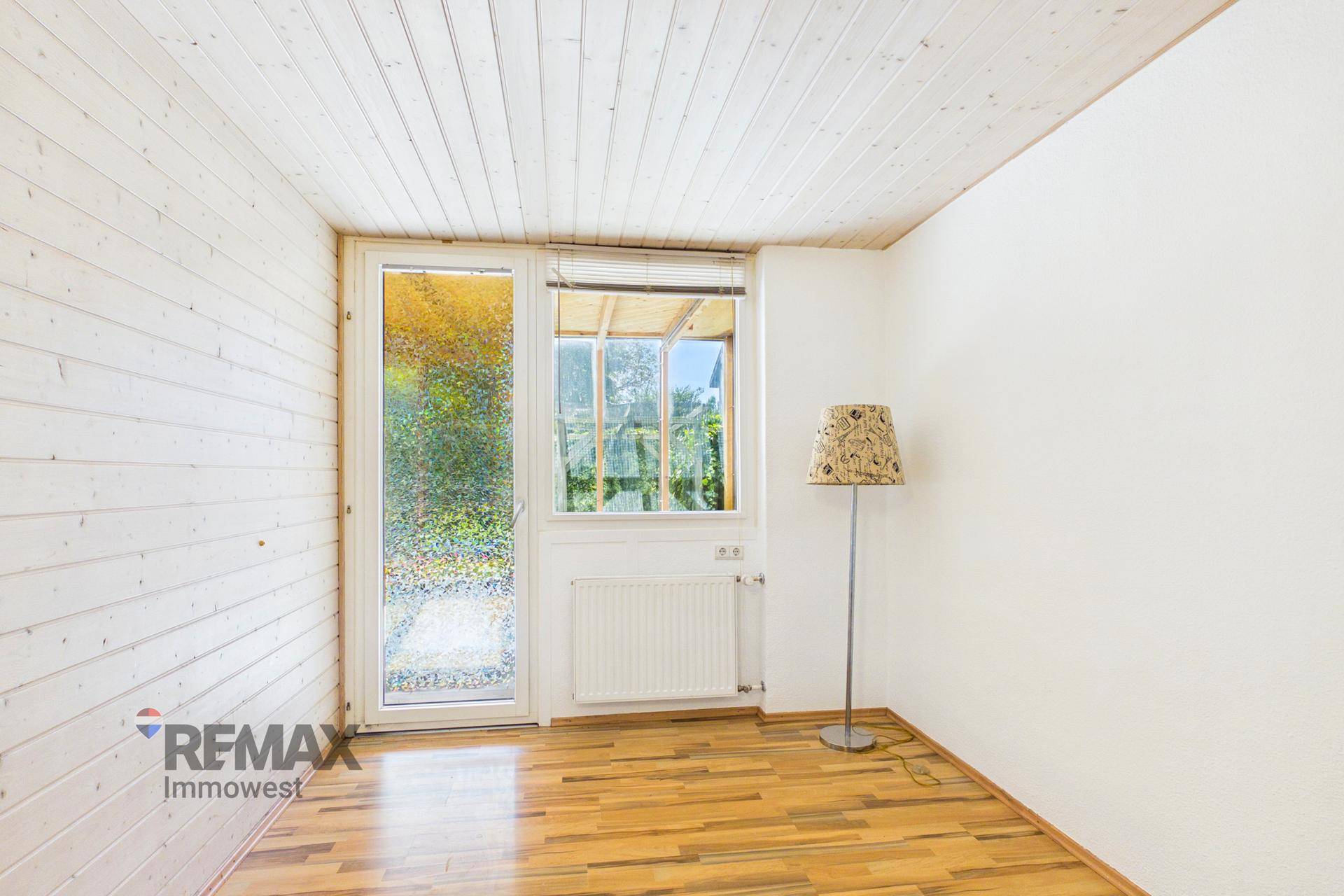 Leerer Raum mit Holzverkleidung, Holzboden und Fenster mit Blick ins Grüne, sehr hell.