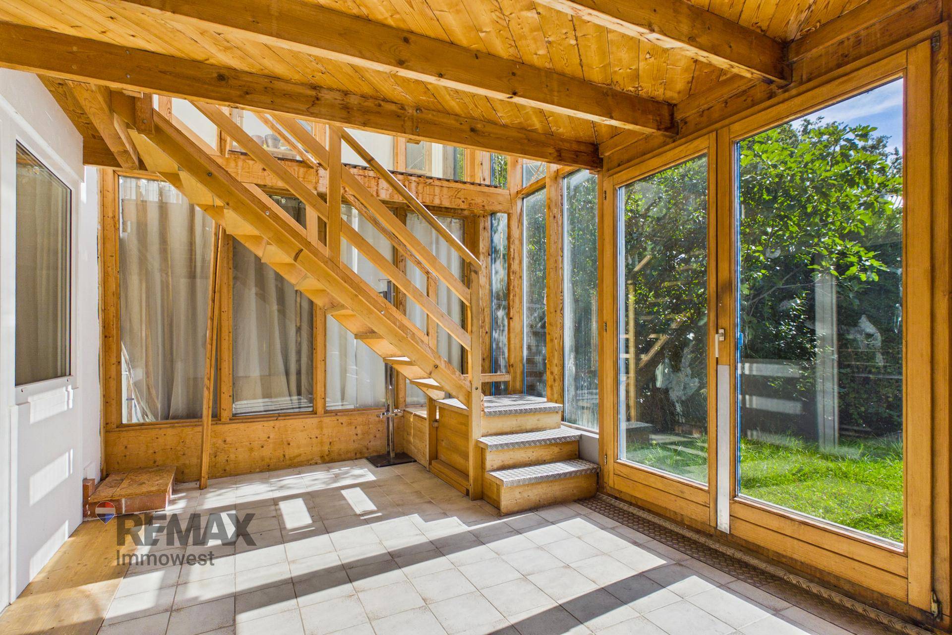 Heller Wintergarten mit Holzkonstruktion, Fliesenboden und Blick in den Garten, ideal zum Entspannen.