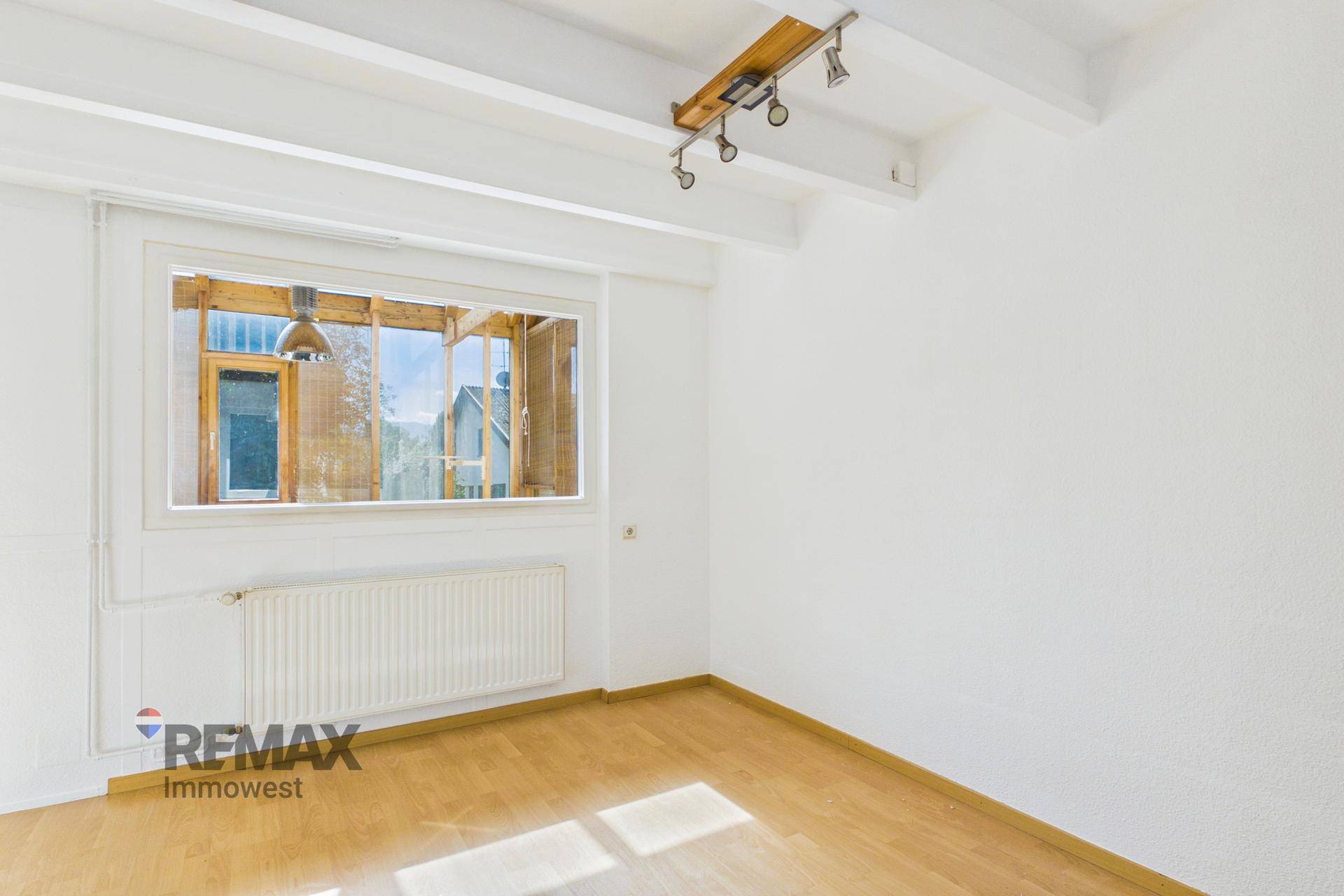 Heller Raum mit Holzboden und großem Fenster, das viel Tageslicht hereinlässt, mit Holzbalkendecke.