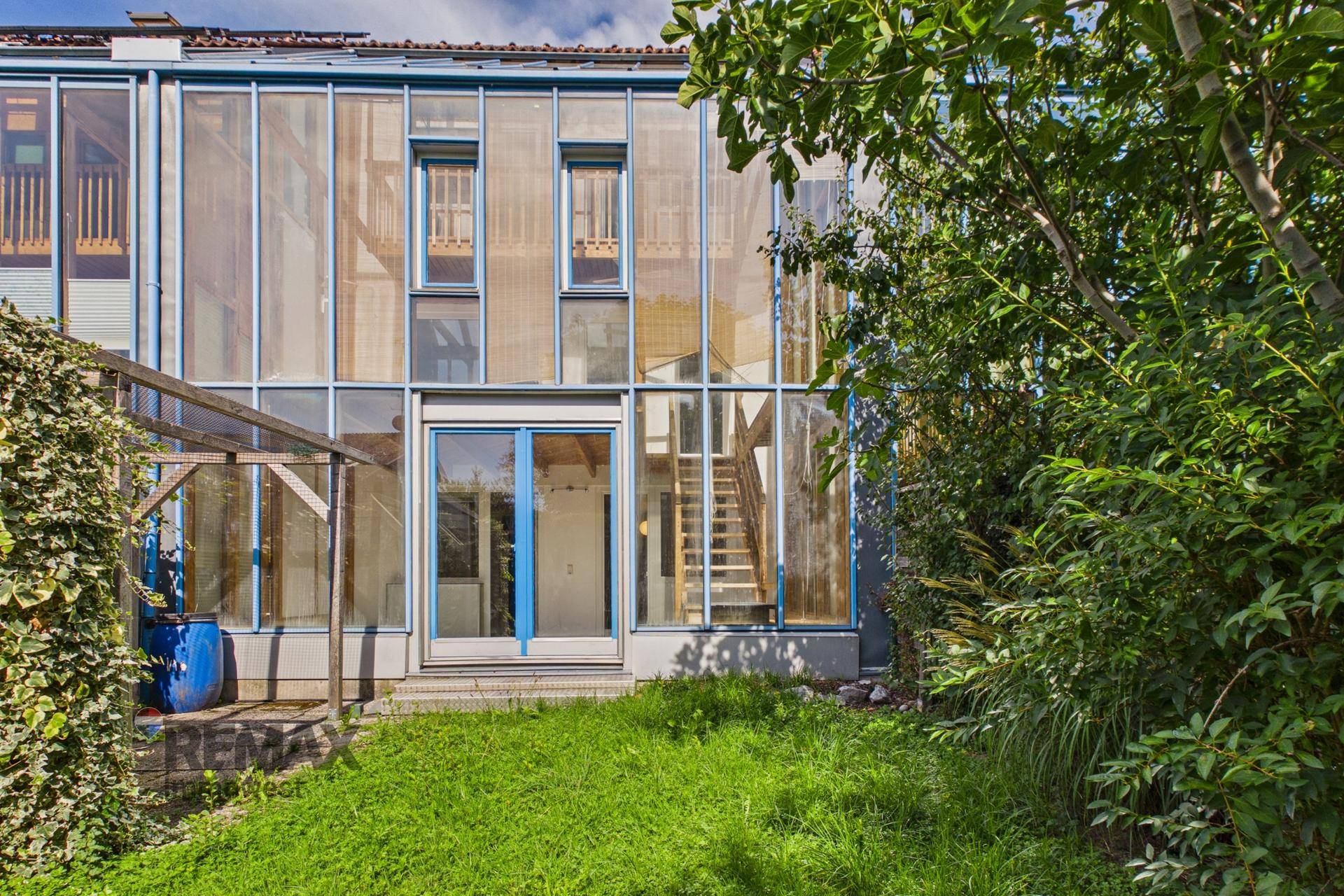 Moderne Glasfassade des Gebäudes mit Gartenbereich und üppiger Vegetation, sehr ansprechend.