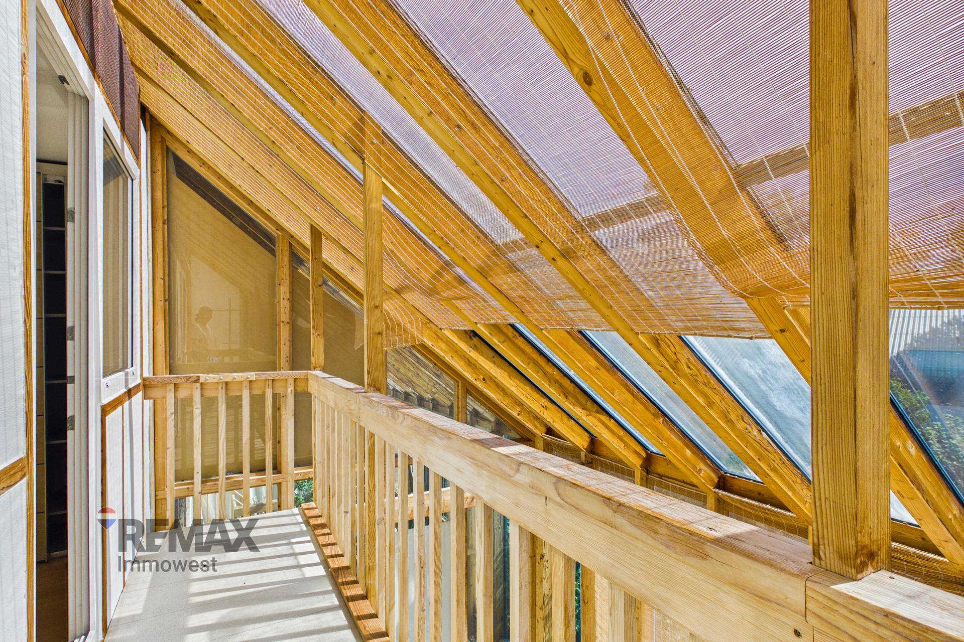 Heller Balkon im Wintergarten mit Holzgeländer und Blick auf die Umgebung, mit viel Tageslicht.