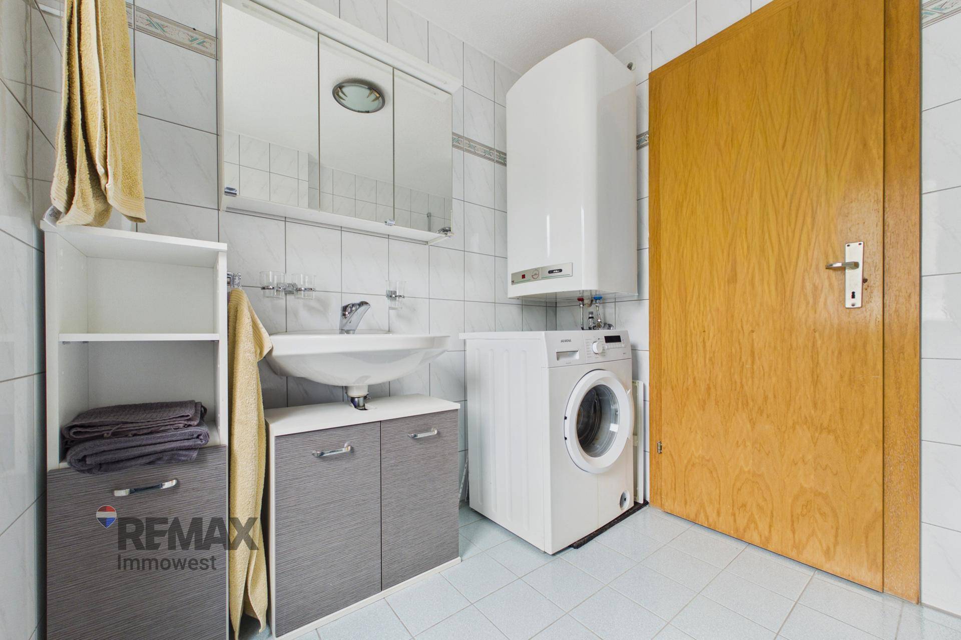 Badezimmer mit Waschbecken, Spiegelschrank, Waschmaschine und Fliesenboden in hellen Farben.