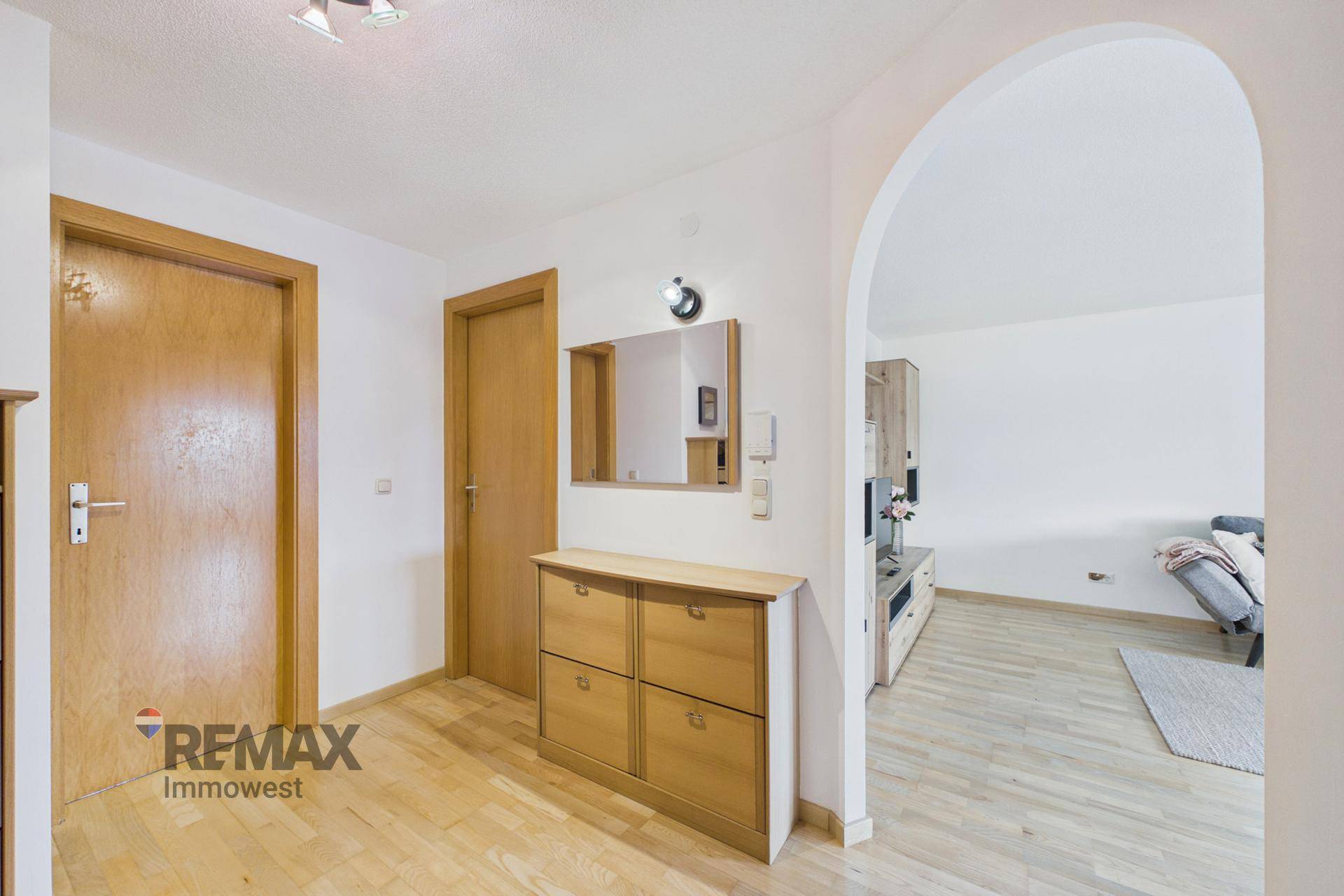 Heller Eingangsbereich mit Holzfußboden, Schuhschrank und einem Bogen zum Wohnbereich.