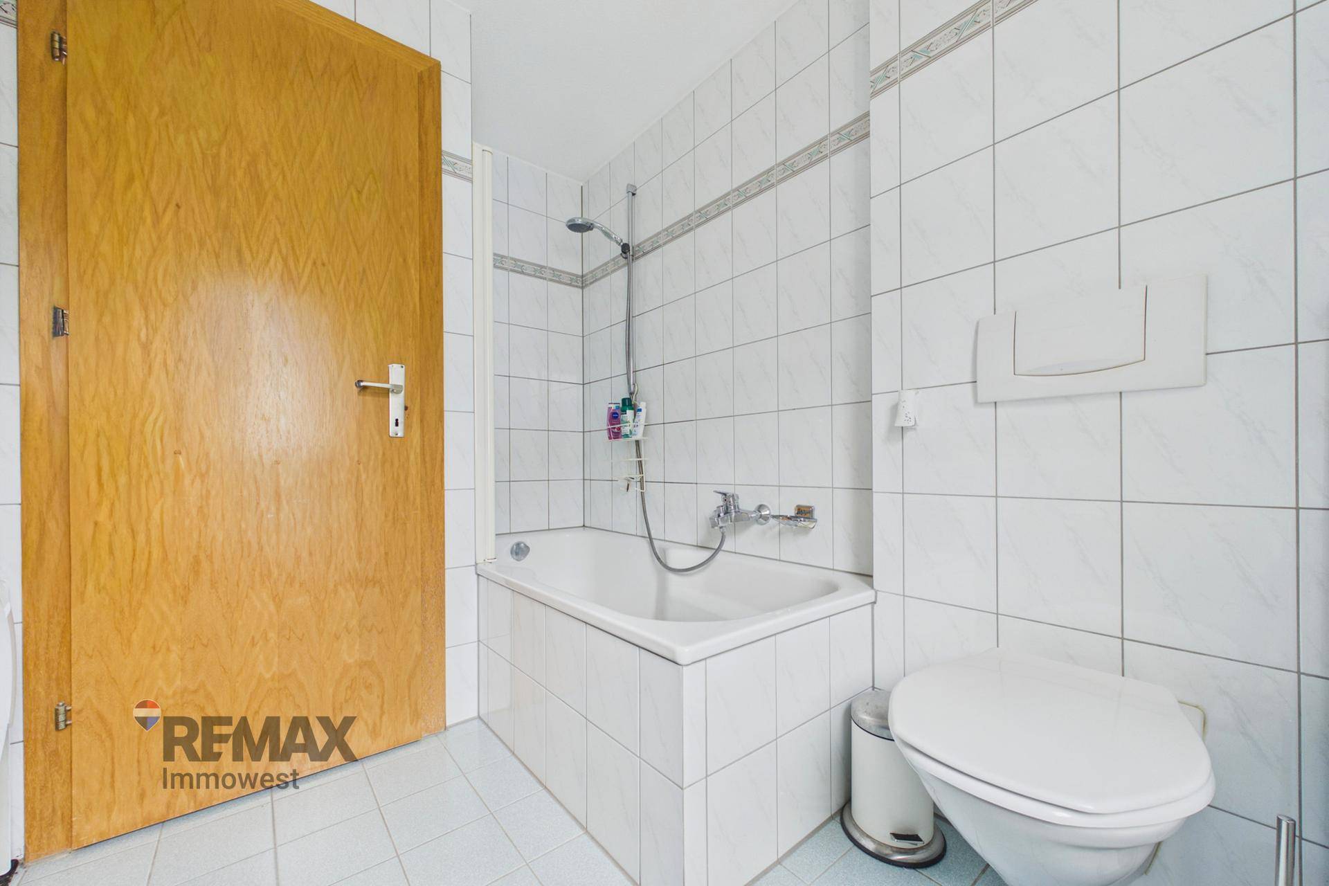 Badezimmer mit Badewanne, Toilette und weißen Fliesen an Wänden und Boden.