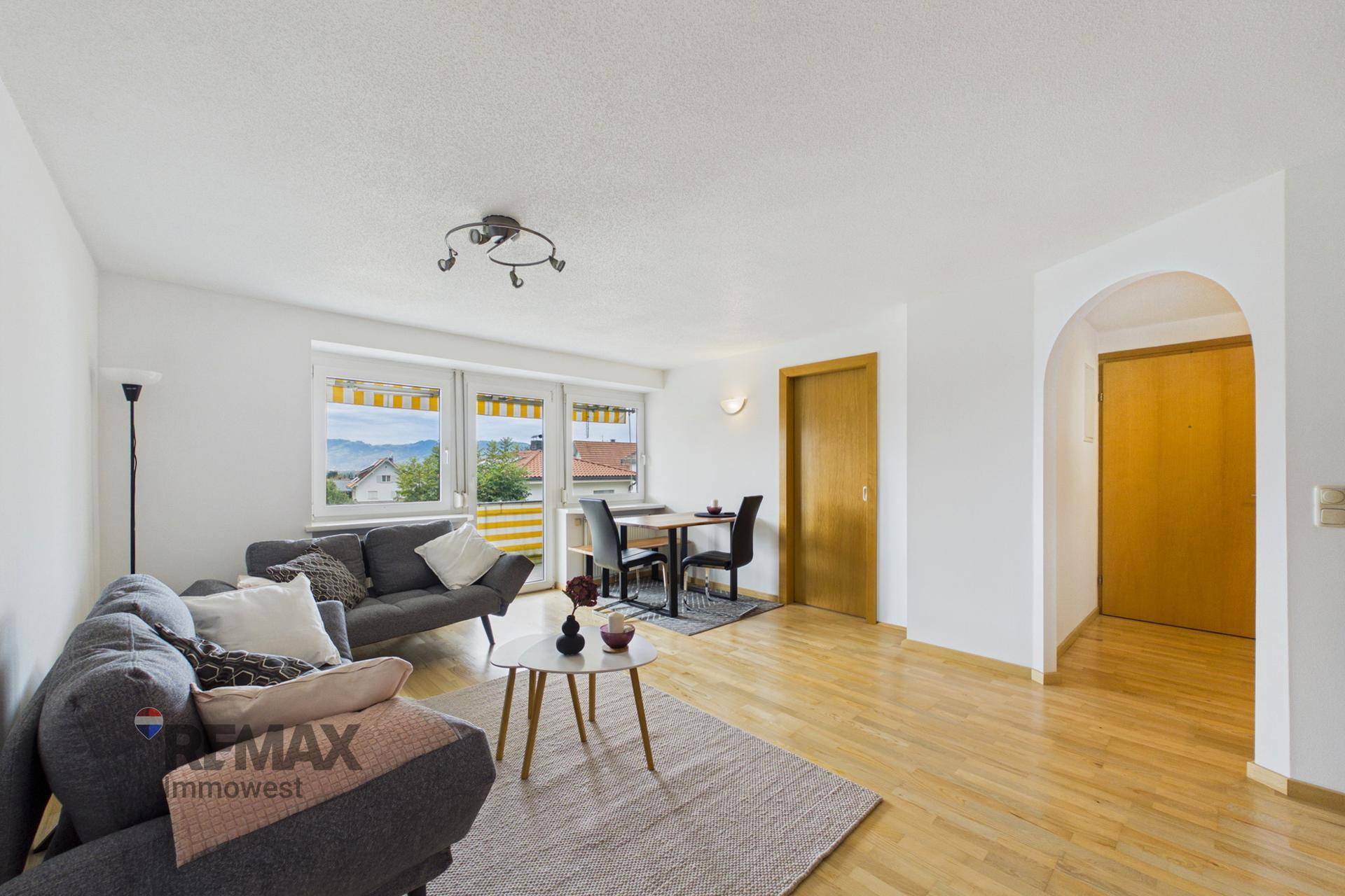 Offener Wohn- und Essbereich mit Holzfußboden, Sofa und Esstisch am Fenster.