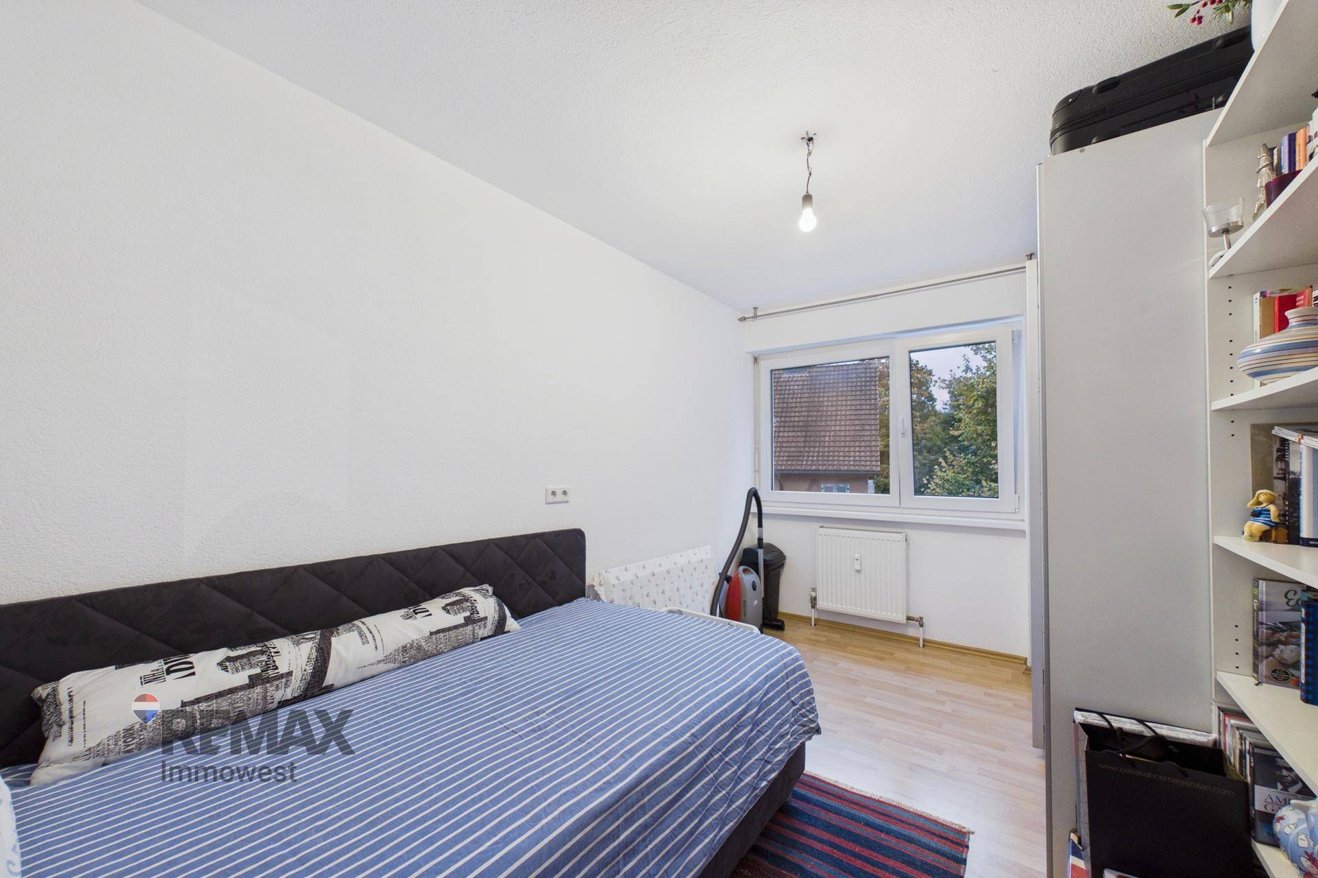Helles Schlafzimmer mit Einzelbett, Holzfußboden und Fenster mit Blick ins Grüne.