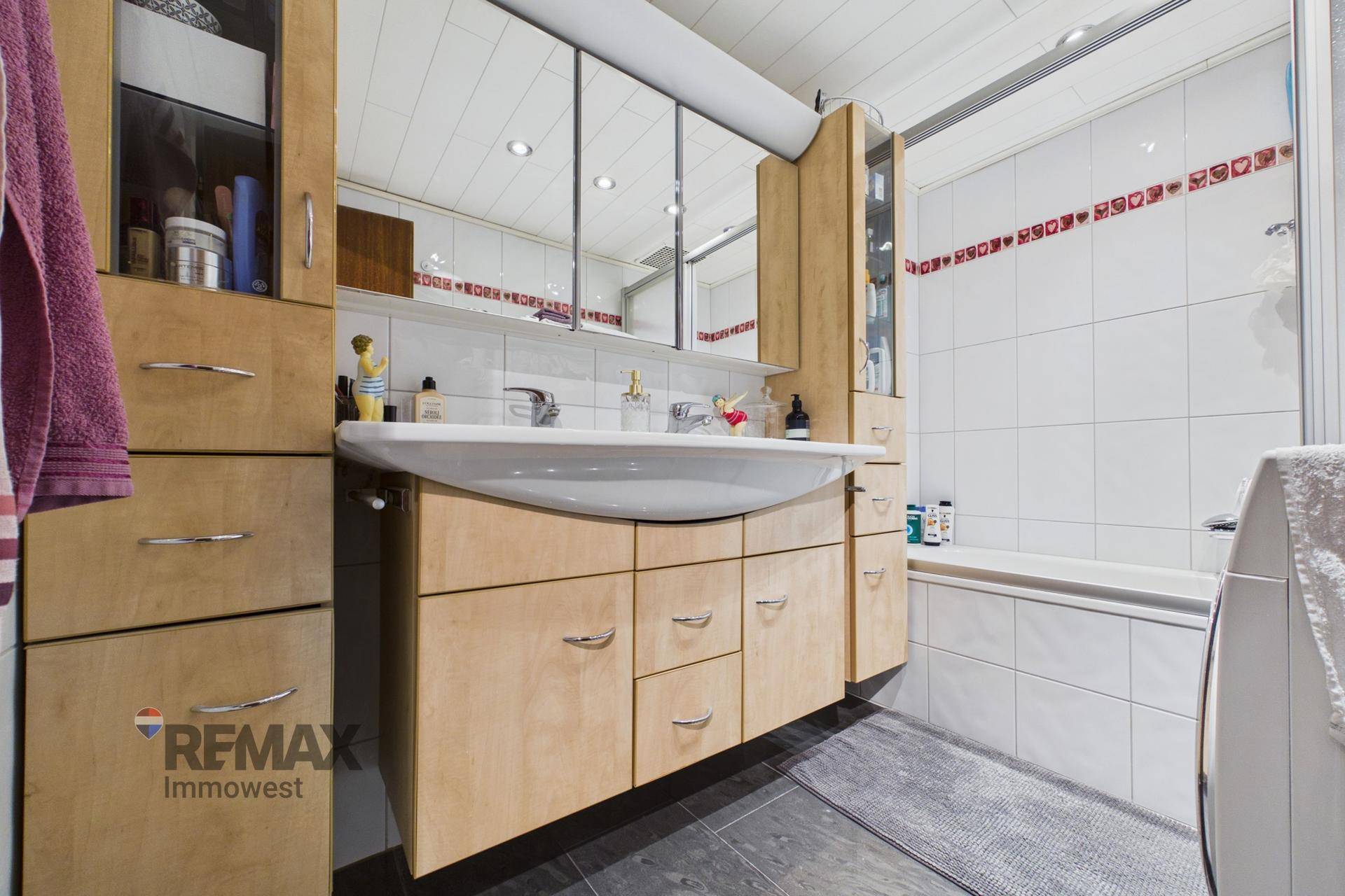 Badezimmer mit Holzschränken, Waschbecken, Spiegelschrank und integrierter Badewanne.