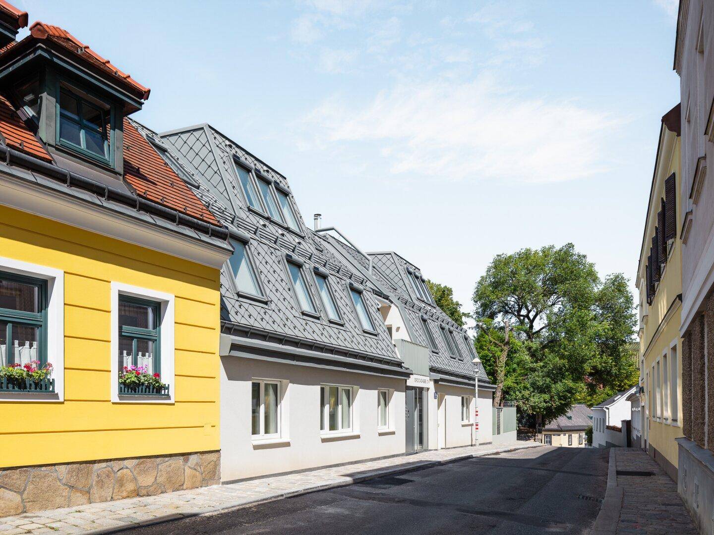 Eine ruhige Wohnstraße mit traditionellen und modernisierten Gebäuden unter einem klaren Himmel.