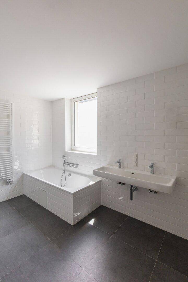 Modernes Badezimmer mit weißer Badewanne, Doppelwaschbecken und großformatigen grauen Fliesen.