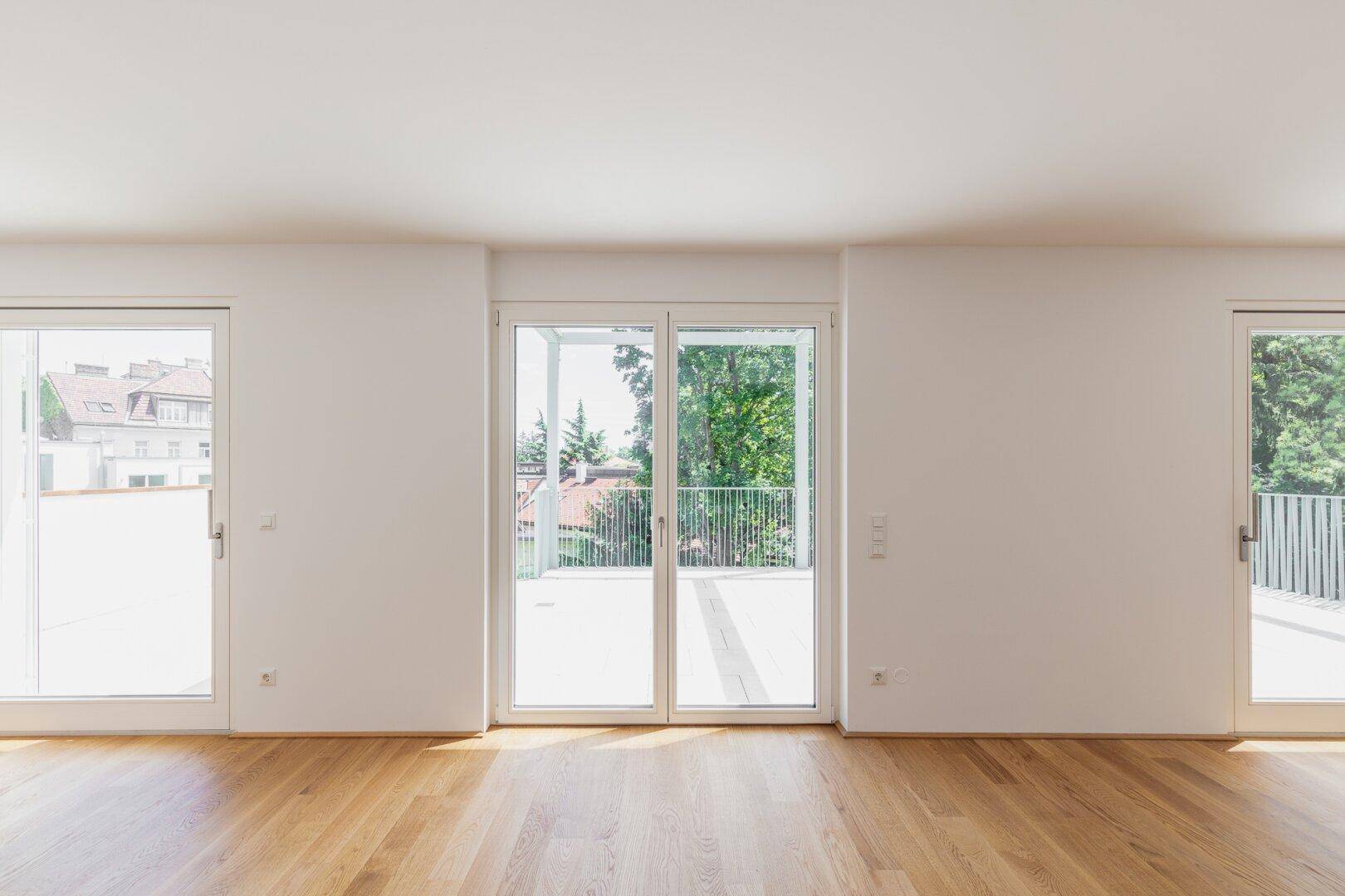 Geräumiger, heller Wohnbereich mit Holzboden und großen Schiebetüren zu einem Balkon.