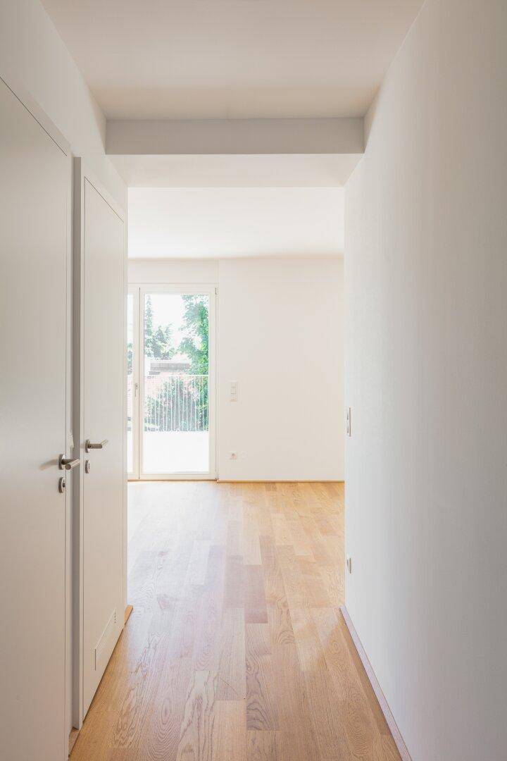 Heller Flur mit Holzboden, der zu einem lichtdurchfluteten Raum mit Balkonzugang führt.