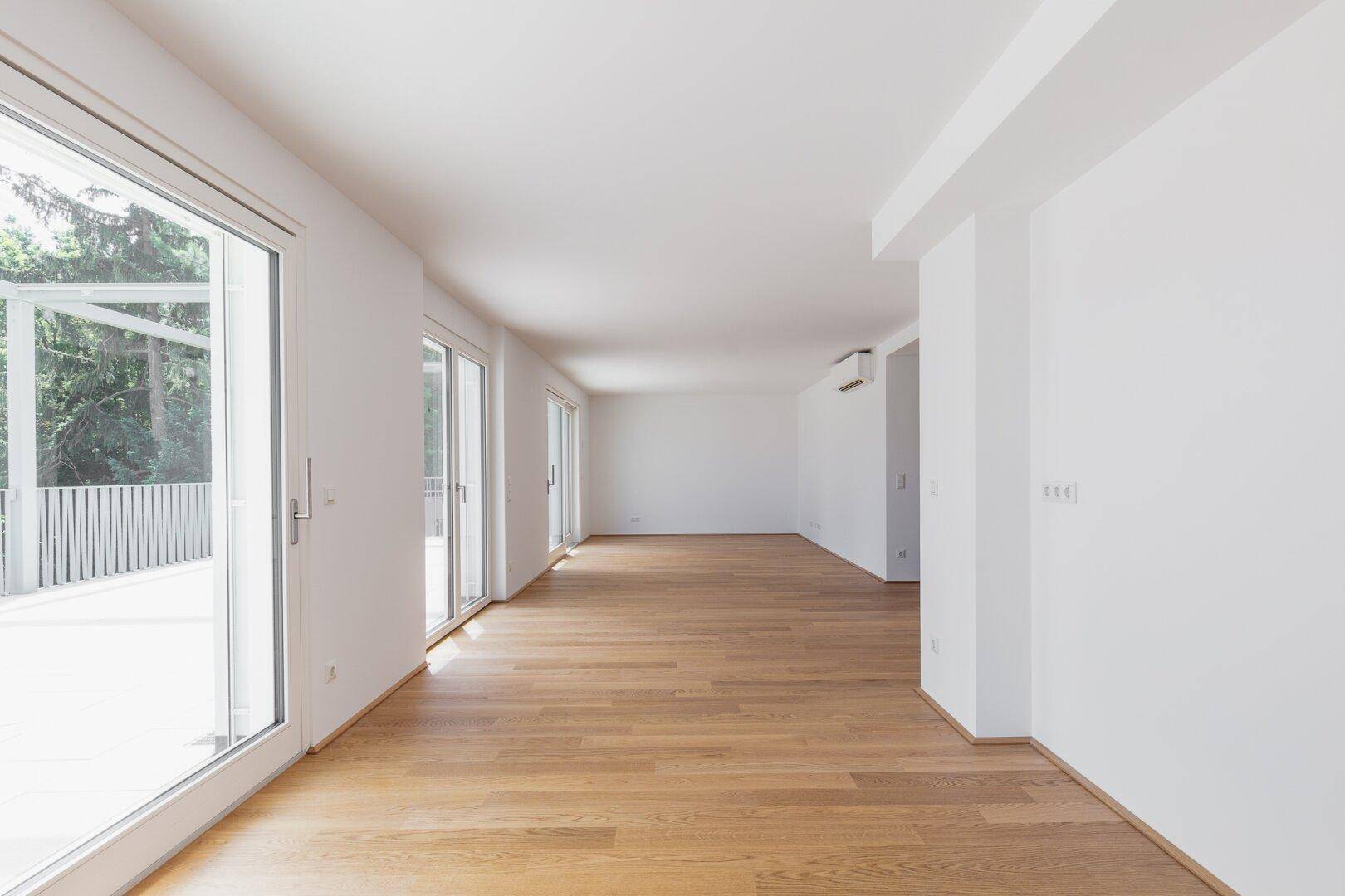 Langer, heller Wohnraum mit Holzboden und mehreren Zugängen zu einer großen Terrasse.