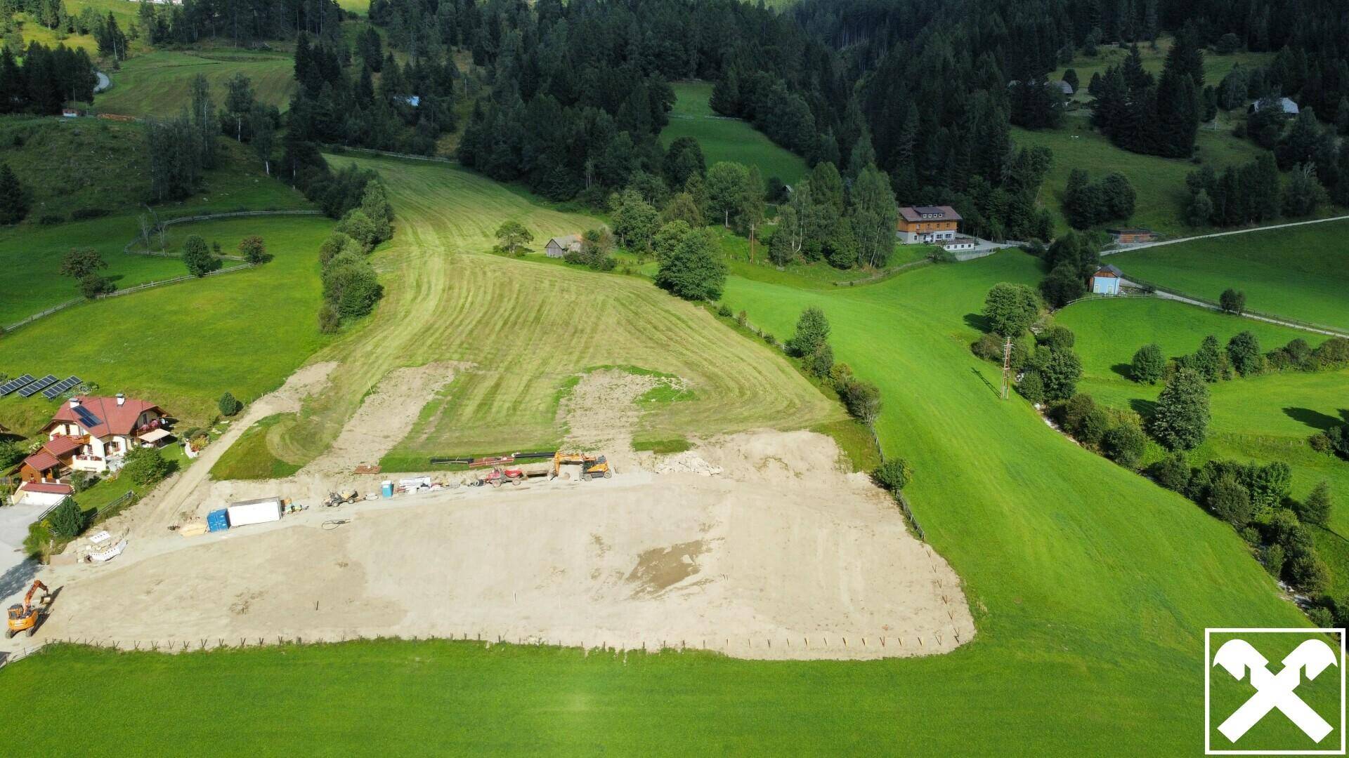 Luftaufnahme eines Baugrundstücks in einer ländlichen Umgebung, umgeben von grünen Wiesen und Wäldern.