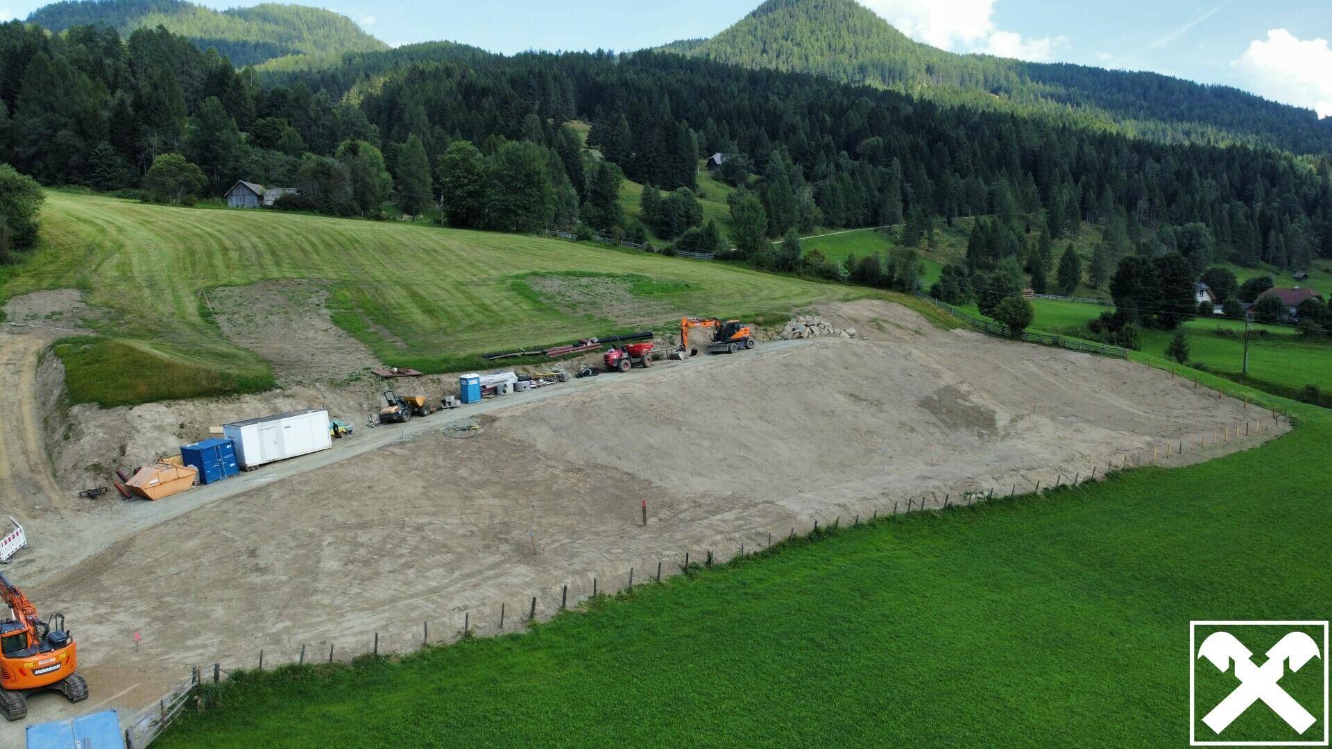 Weitläufiges Baugrundstück mit Erdarbeiten und Baumaschinen, umgeben von einer natürlichen Landschaft.
