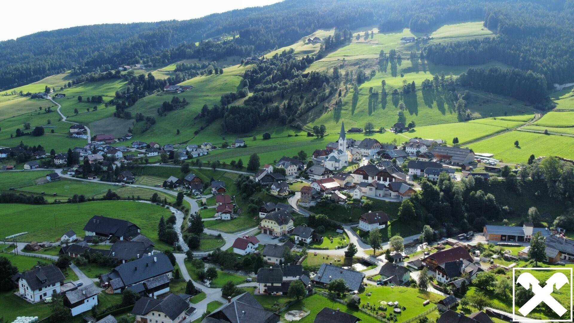 Panoramablick auf ein idyllisches Dorf, eingebettet in sanfte grüne Hügel und umgeben von Natur.