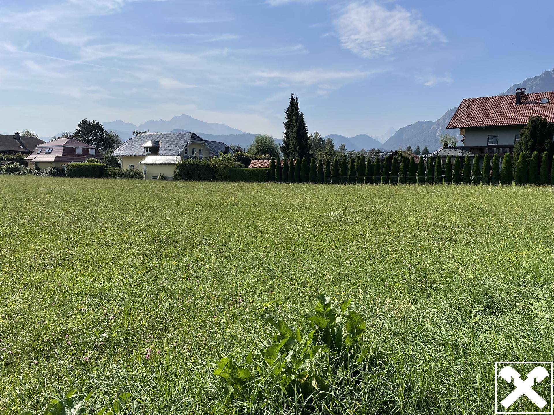 Sonnige Grünfläche mit angrenzenden Häusern und Panoramablick auf die Berglandschaft.