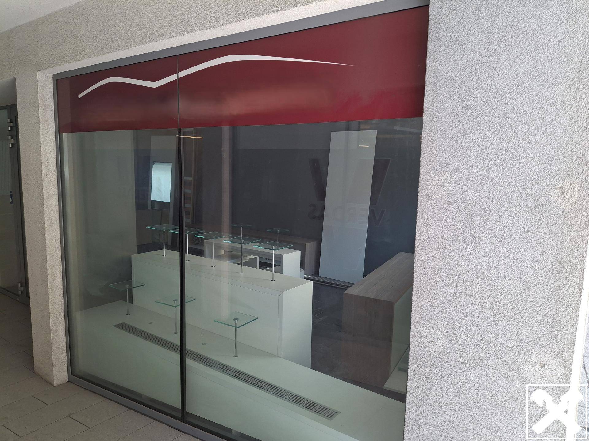 Außenansicht des Geschäfts mit großer Glasfront und roter Markise, die den Eingangsbereich schützt.