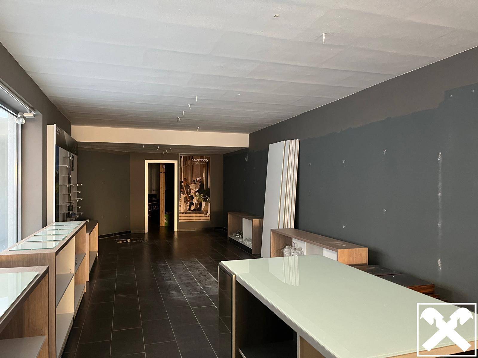 Weiterer Blick in den Ladenraum mit dunklem Fliesenboden und einer leeren Wand, die auf Gestaltung wartet.