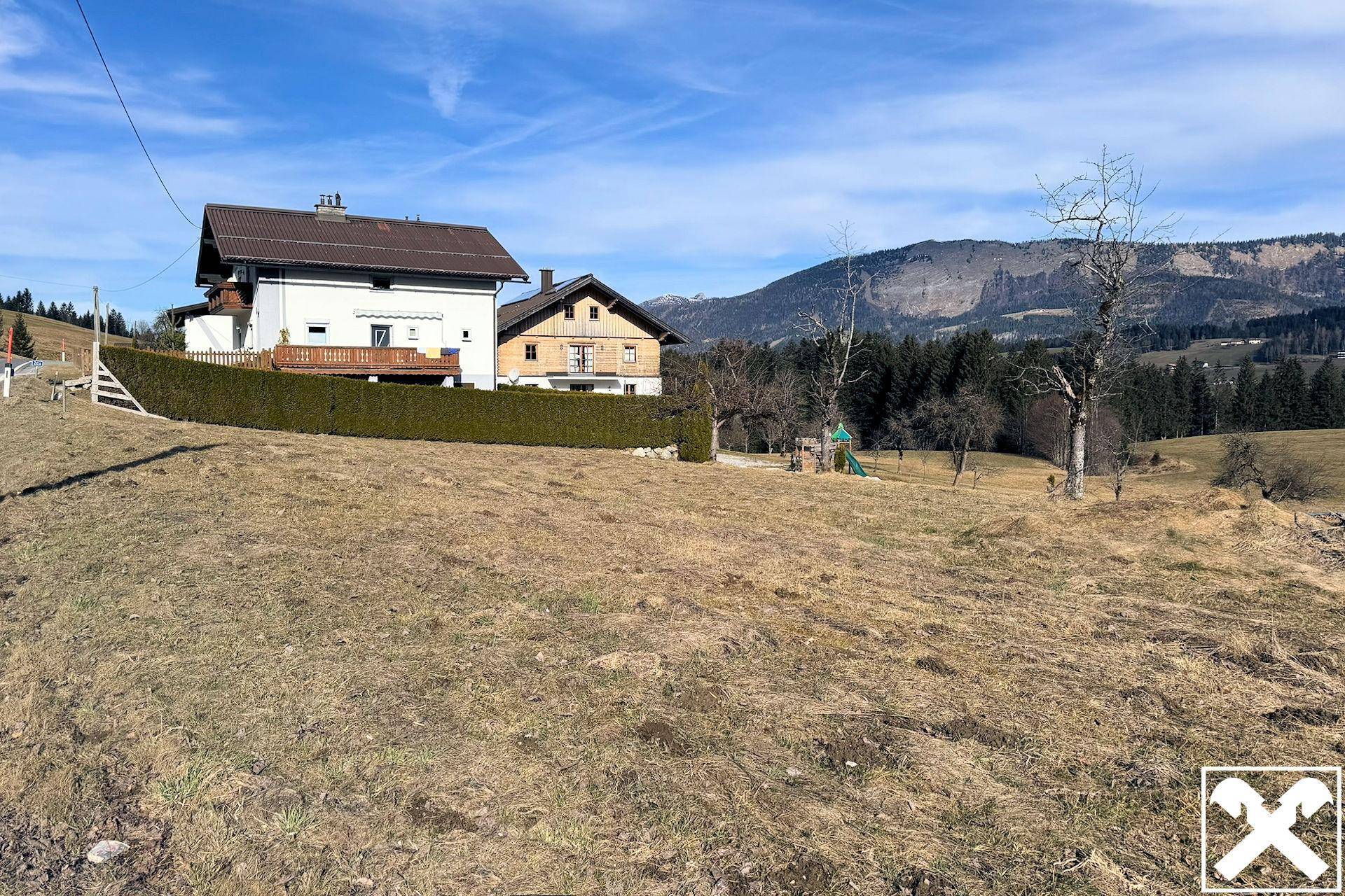 Zwei Wohnhäuser mit gepflegter Hecke und Bergblick, eingebettet in die ländliche Umgebung.