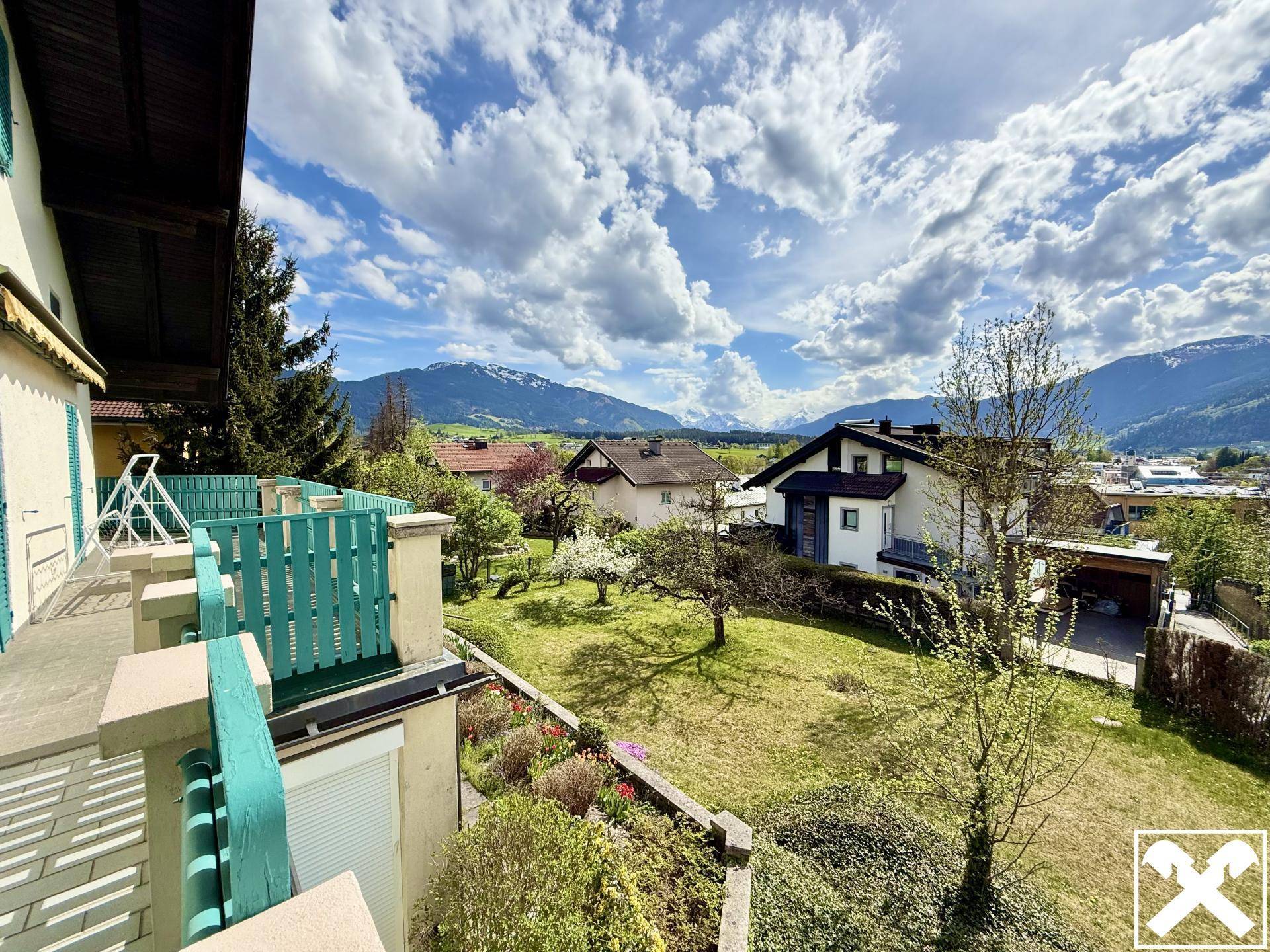 Blick vom Balkon über den Garten auf die umliegenden Häuser und die majestätische Berglandschaft.