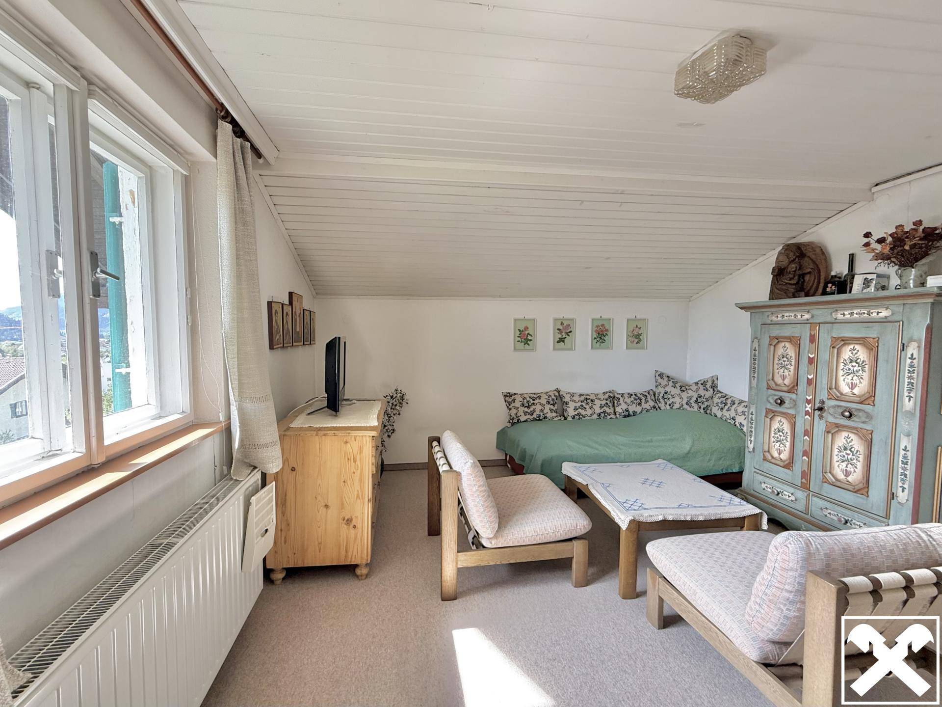 Gemütliches Dachzimmer mit schräger Decke, Tagesbett und traditionell bemalten Möbeln.