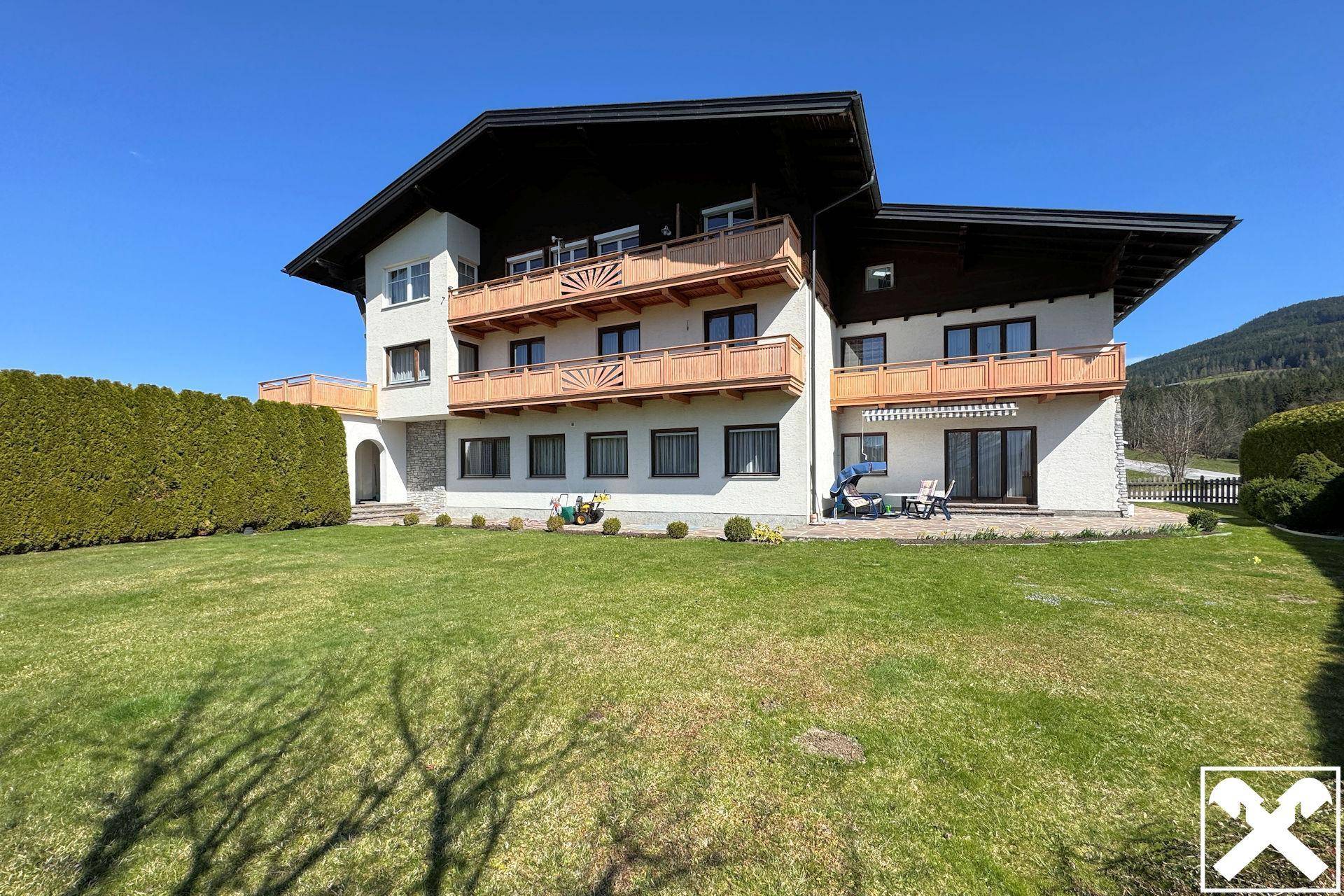 Traditionelles Haus mit mehreren Balkonen und gepflegtem Rasen in alpiner Umgebung.