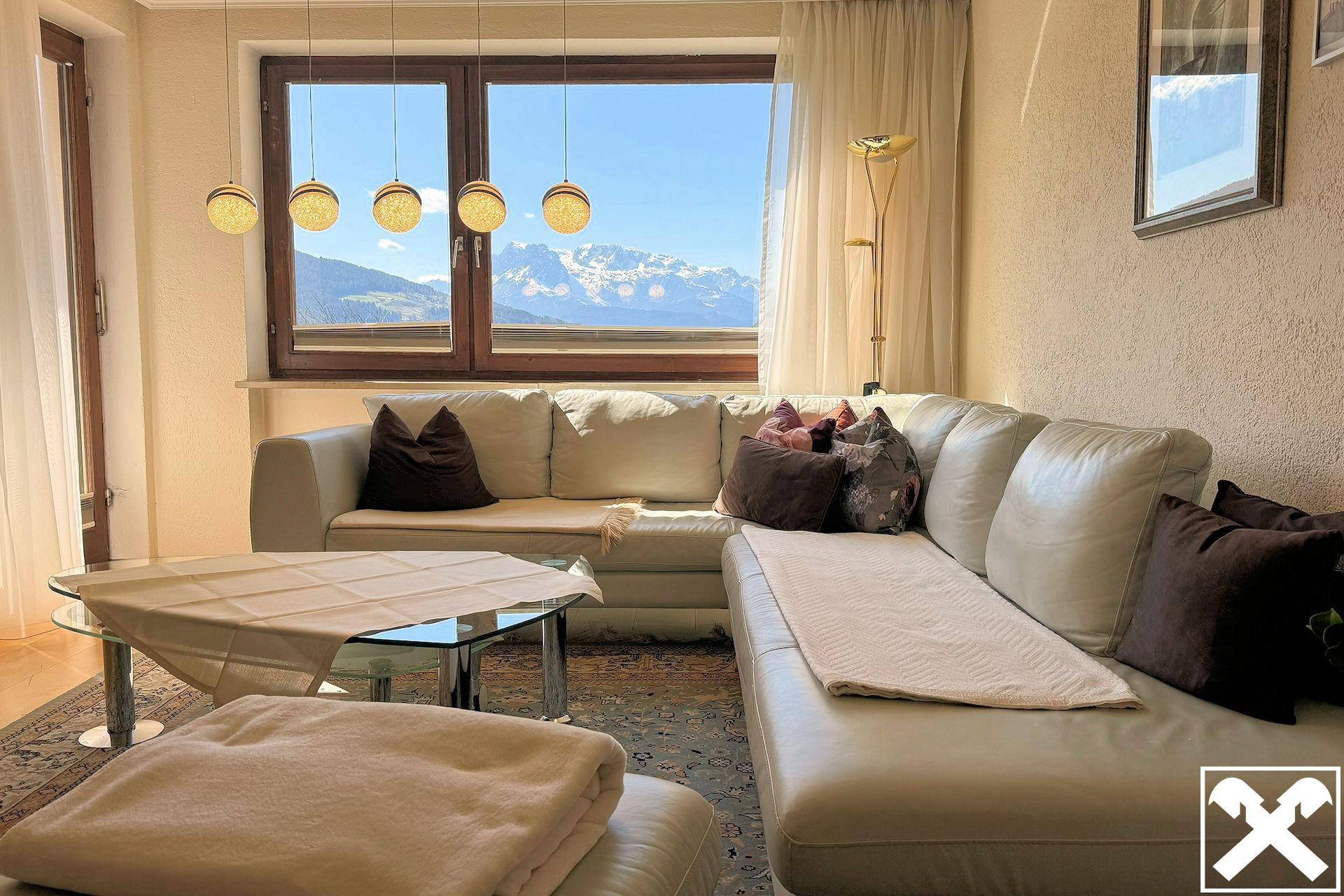 Gemütliches Wohnzimmer mit beigem Sofa, Teppich und Panoramablick auf die Berge.