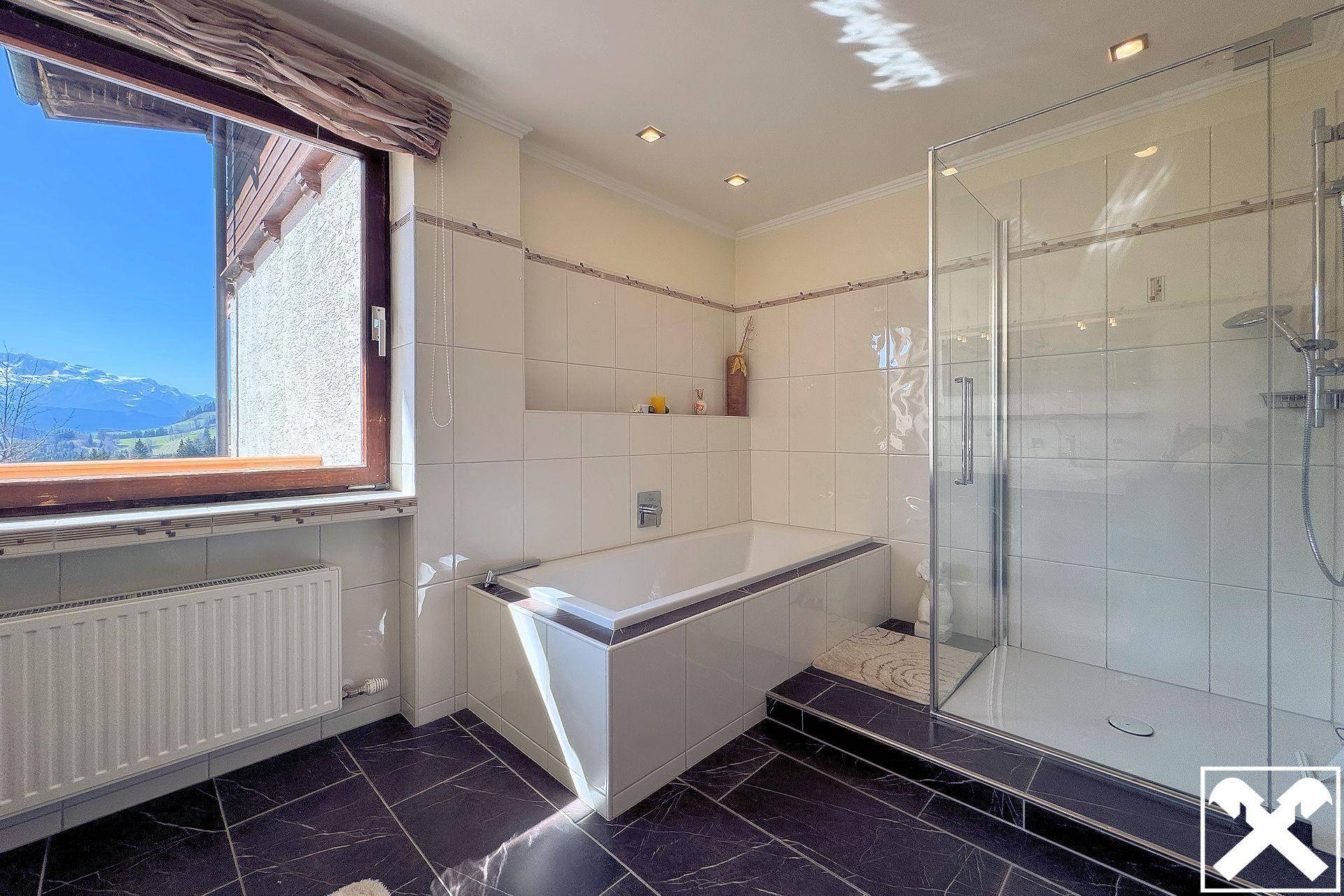 Modernes Badezimmer mit Badewanne, Duschkabine, dunklen Fliesen und Fenster mit Bergblick.