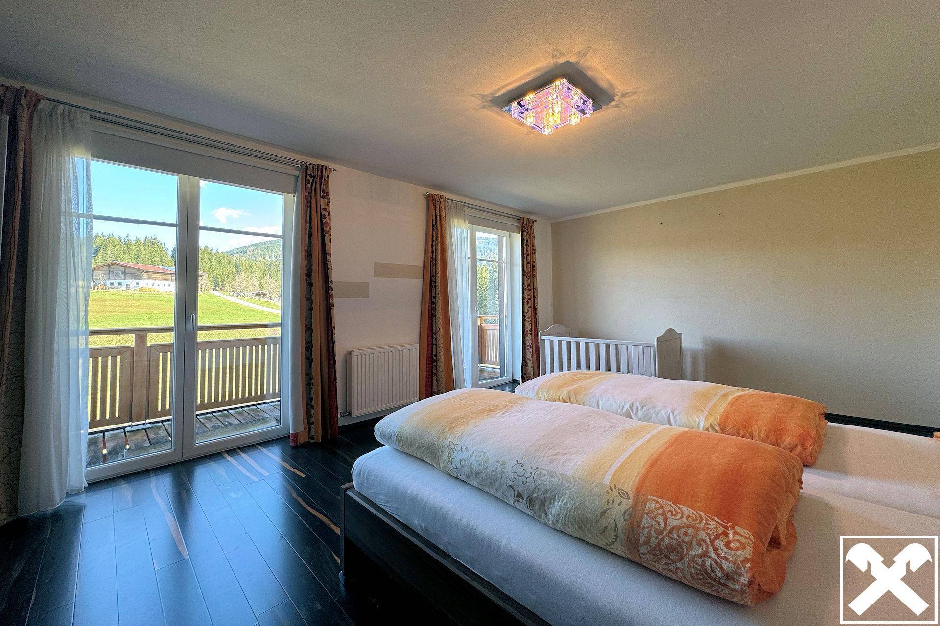 Helles Schlafzimmer mit dunklem Holzboden, Zugang zum Balkon und Blick ins Grüne.
