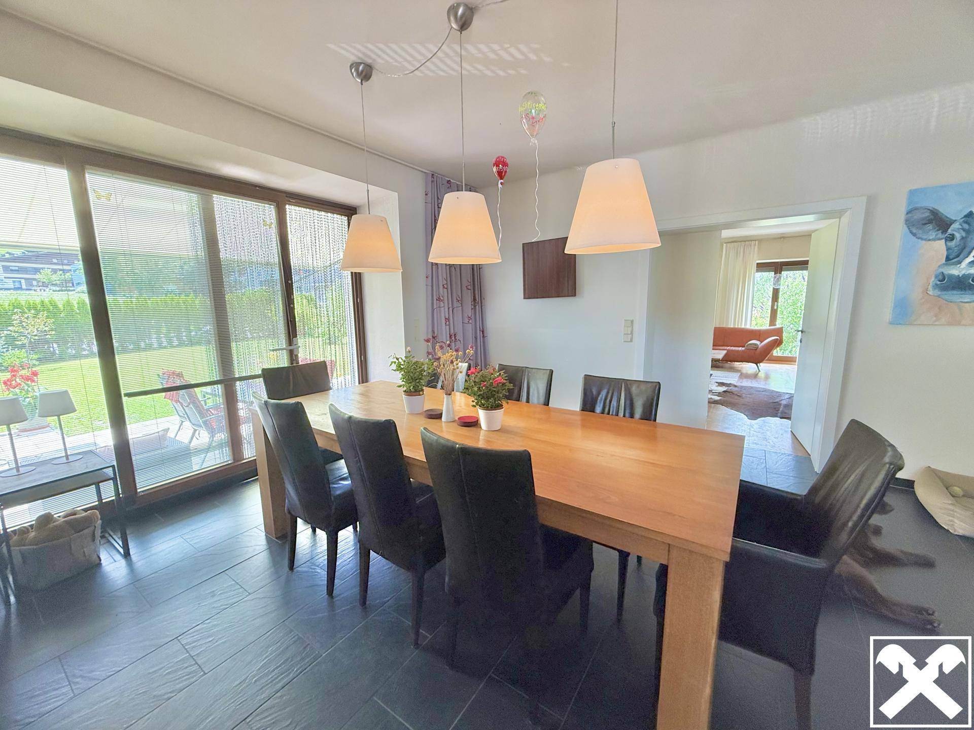 Geräumiges Esszimmer mit großem Holztisch und direktem Zugang zur Terrasse durch breite Glasfronten.